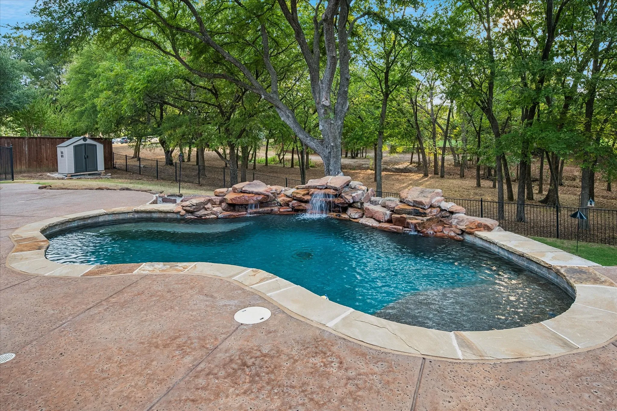 Backyard truly an oasis featuring a pool with fountain, outdoor kitchen, and covered living area overlooking lush green space.
