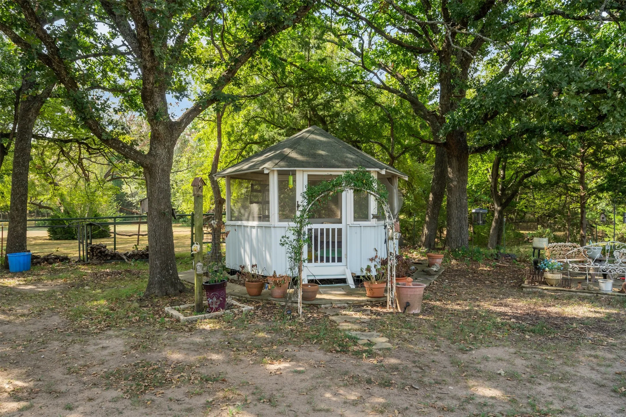 Hexagonal screened gazebo with a pitched roof, surrounded by mature trees