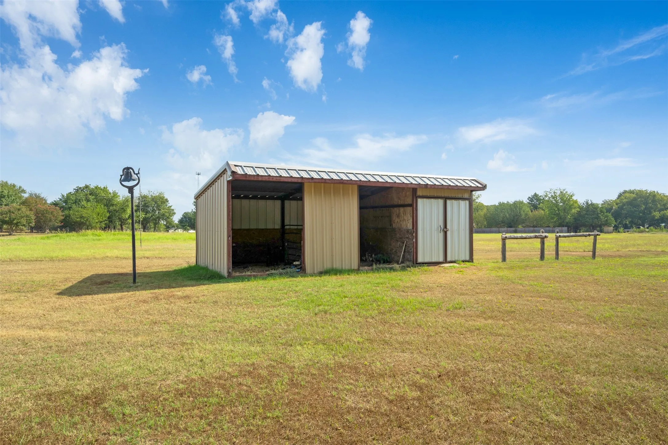 Metal outbuilding with a partially enclosed bay, double doors, and a corrugated metal roof