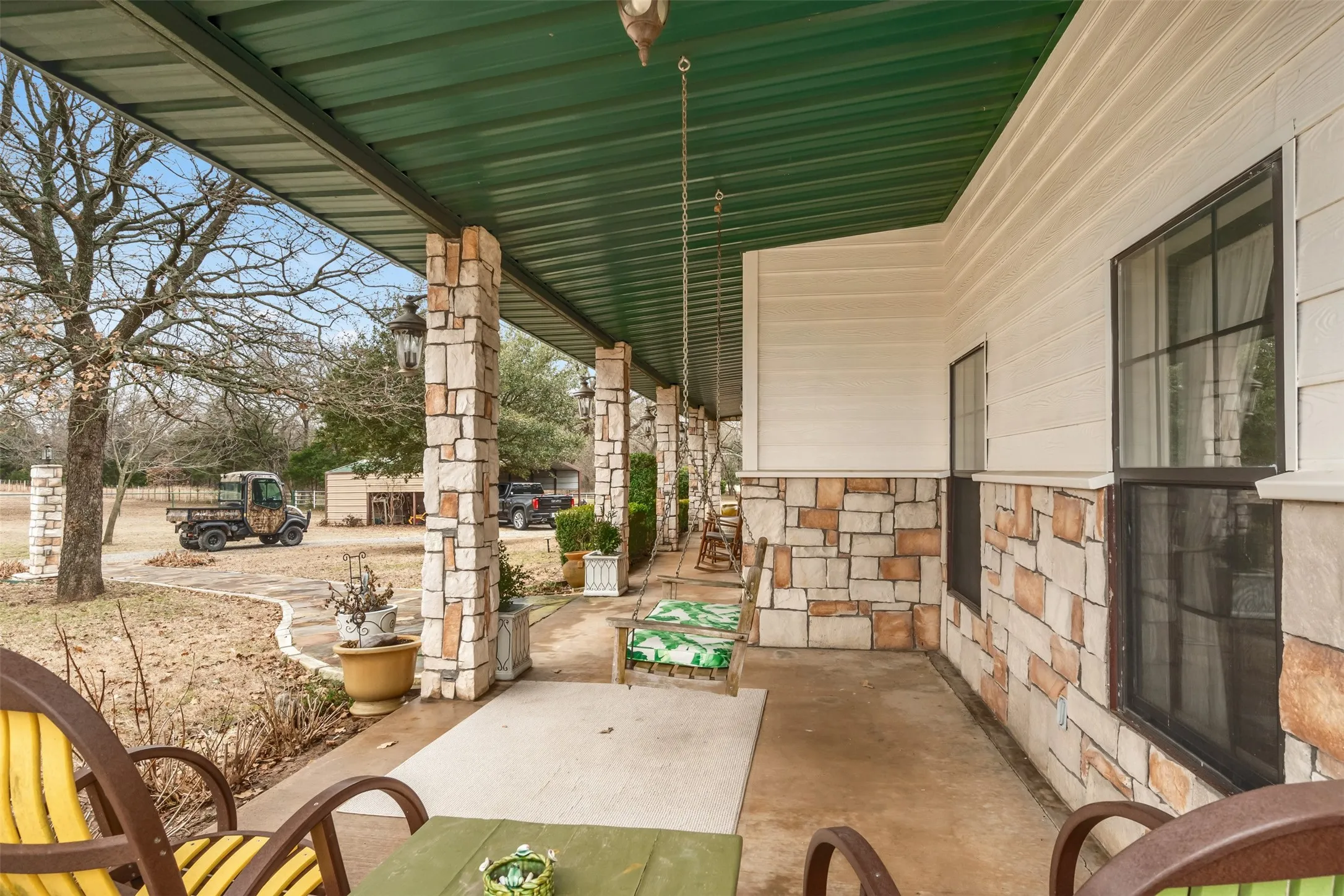 Covered porch featuring stone-clad pillars, a green metal roof, and horizontal siding