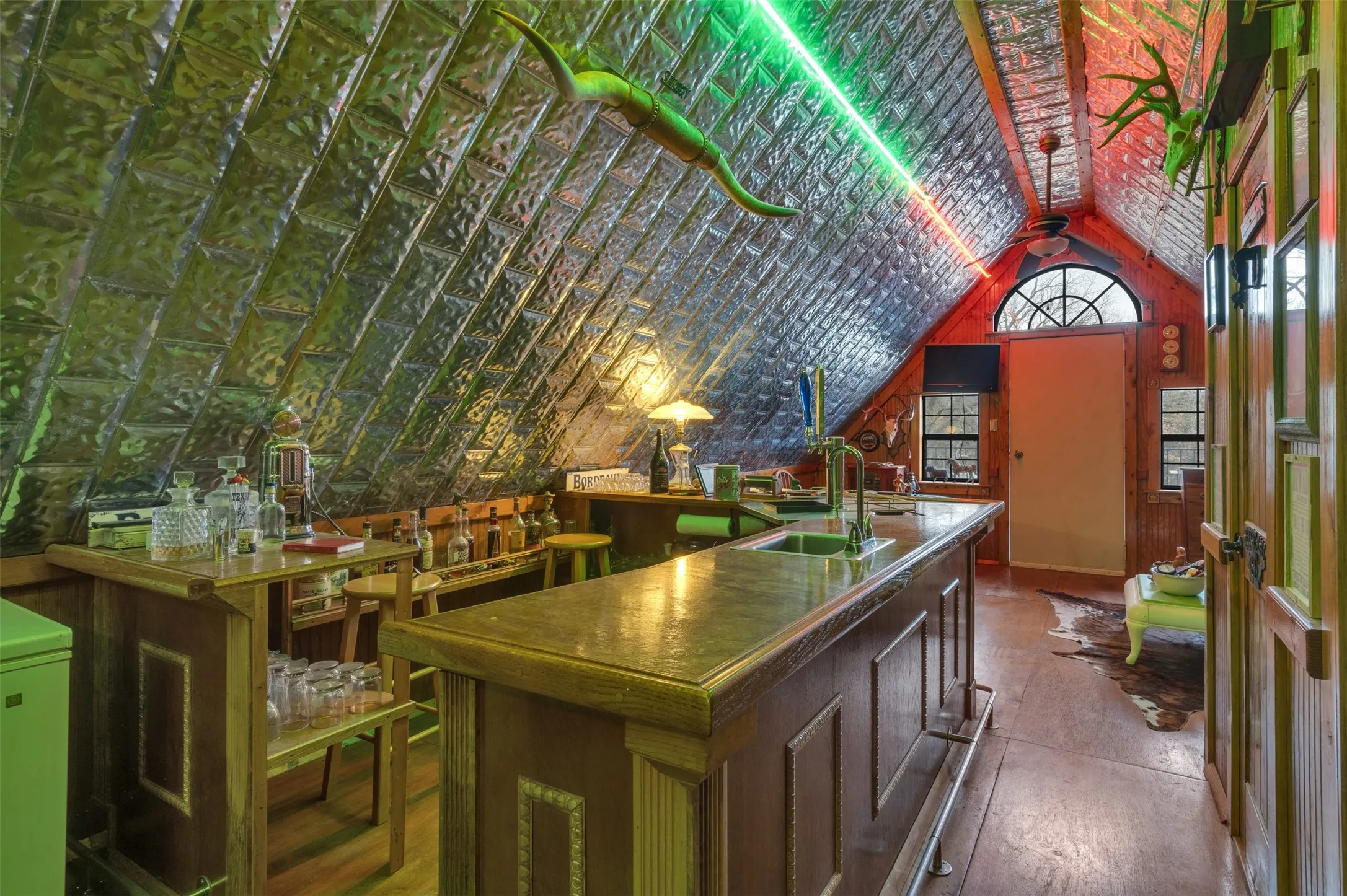 Attic space featuring an arched window, a built-in bar, and wood-finish flooring