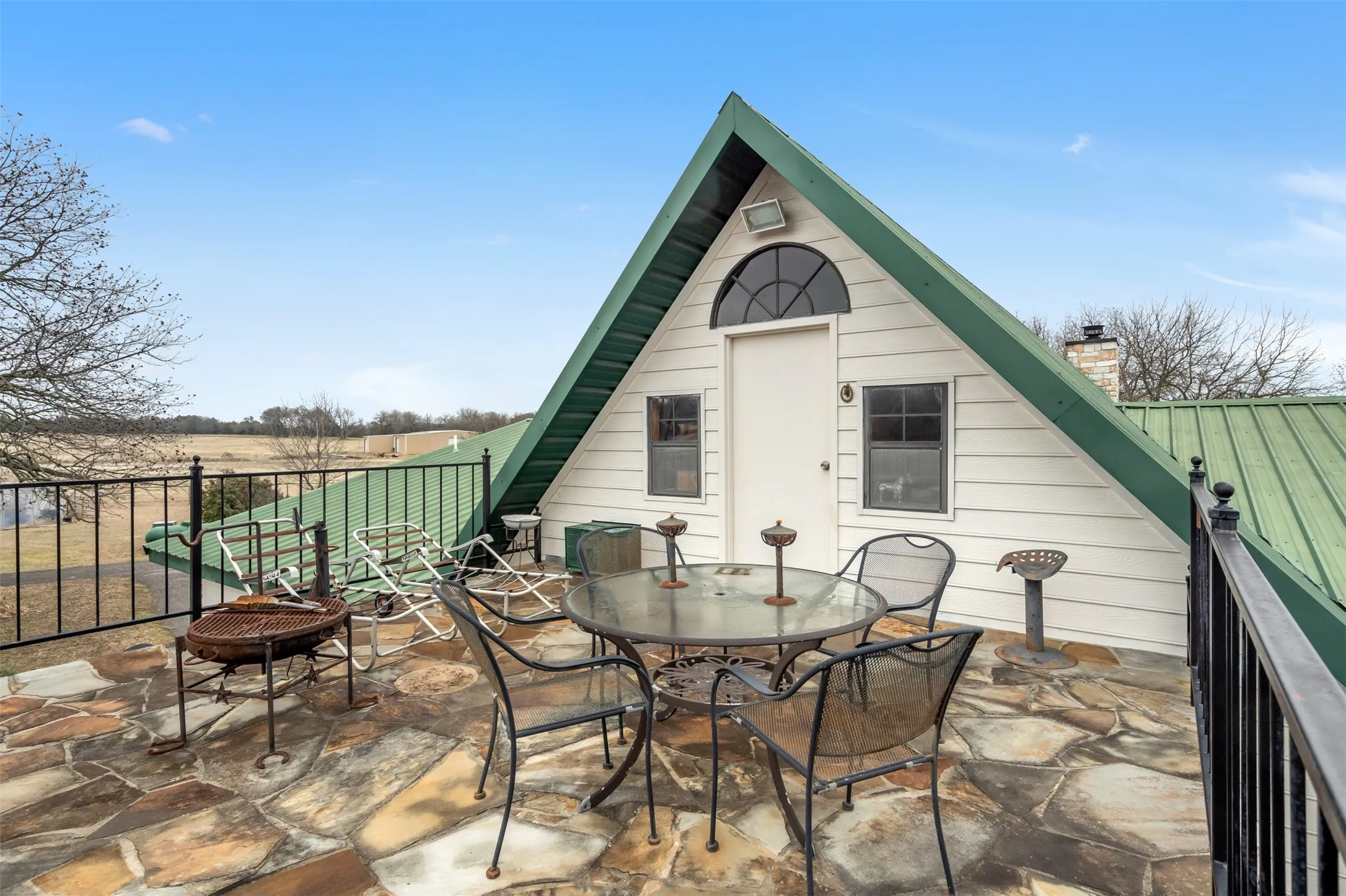 Expansive flagstone patio area with black metal railing and a green metal roof structure