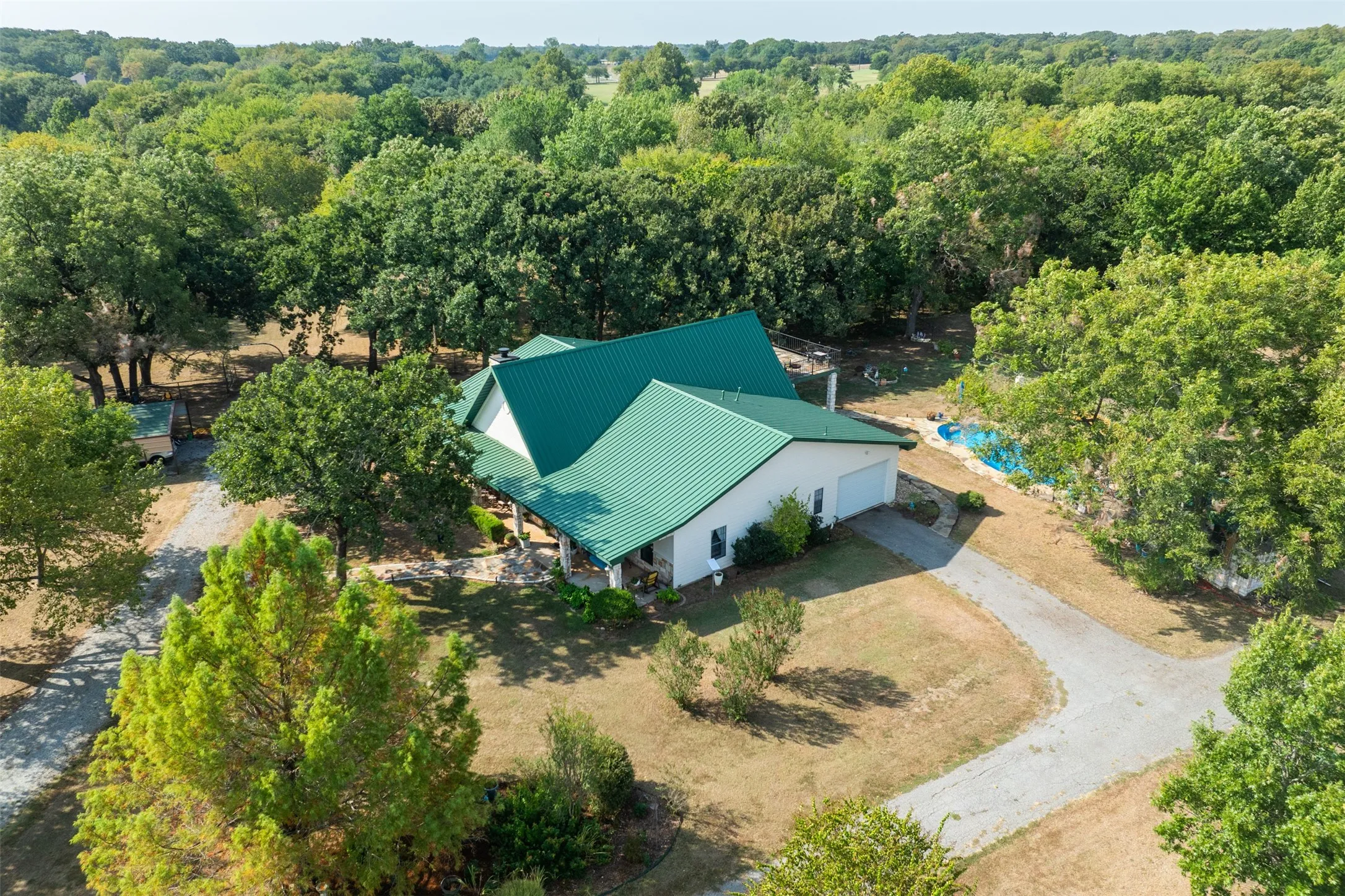 Expansive property featuring a green metal roof, a gravel driveway, a detached garage, and a swimming pool