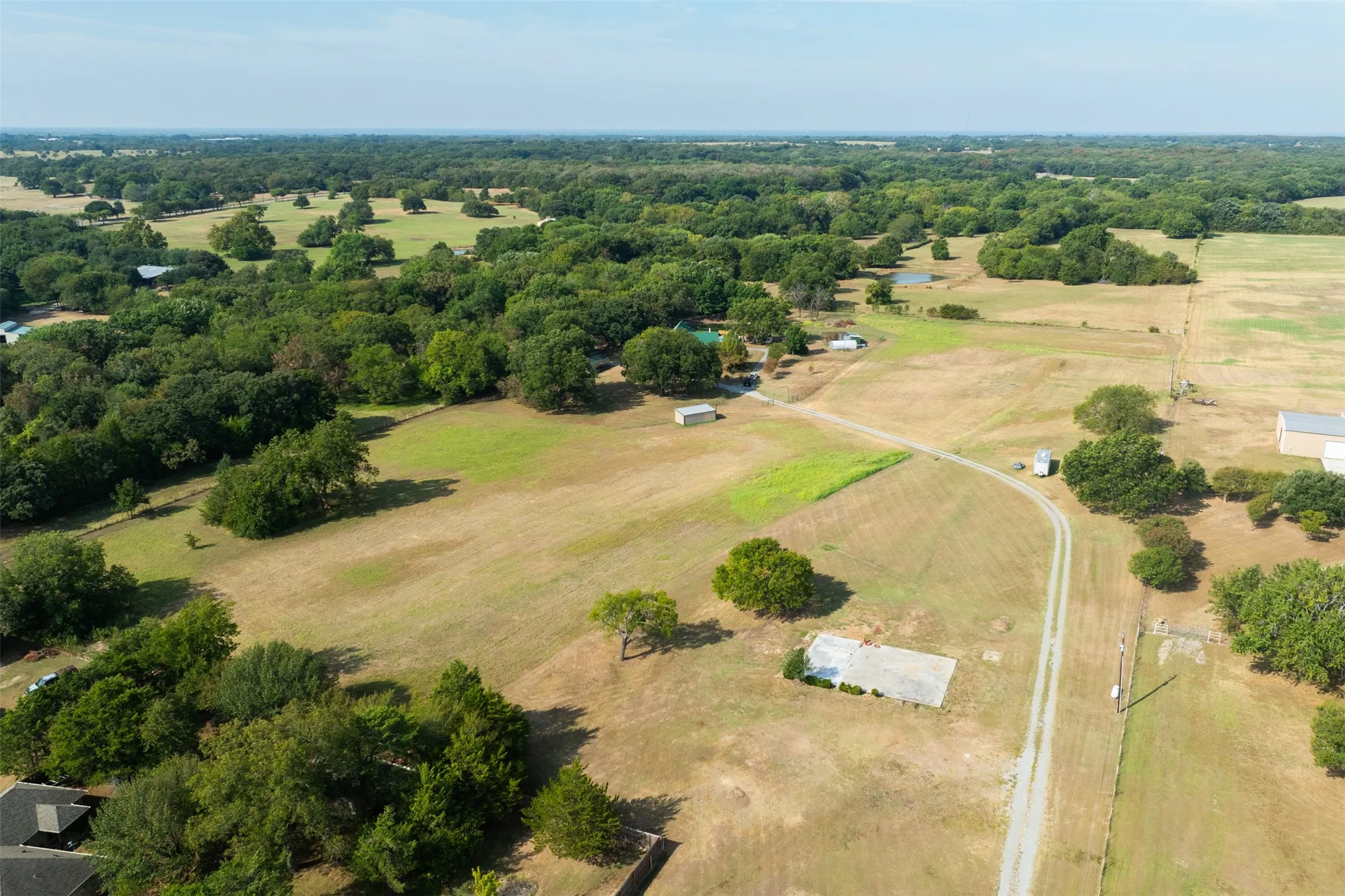 Expansive rural property featuring an unpaved access road, scattered mature trees, and multiple outbuildings