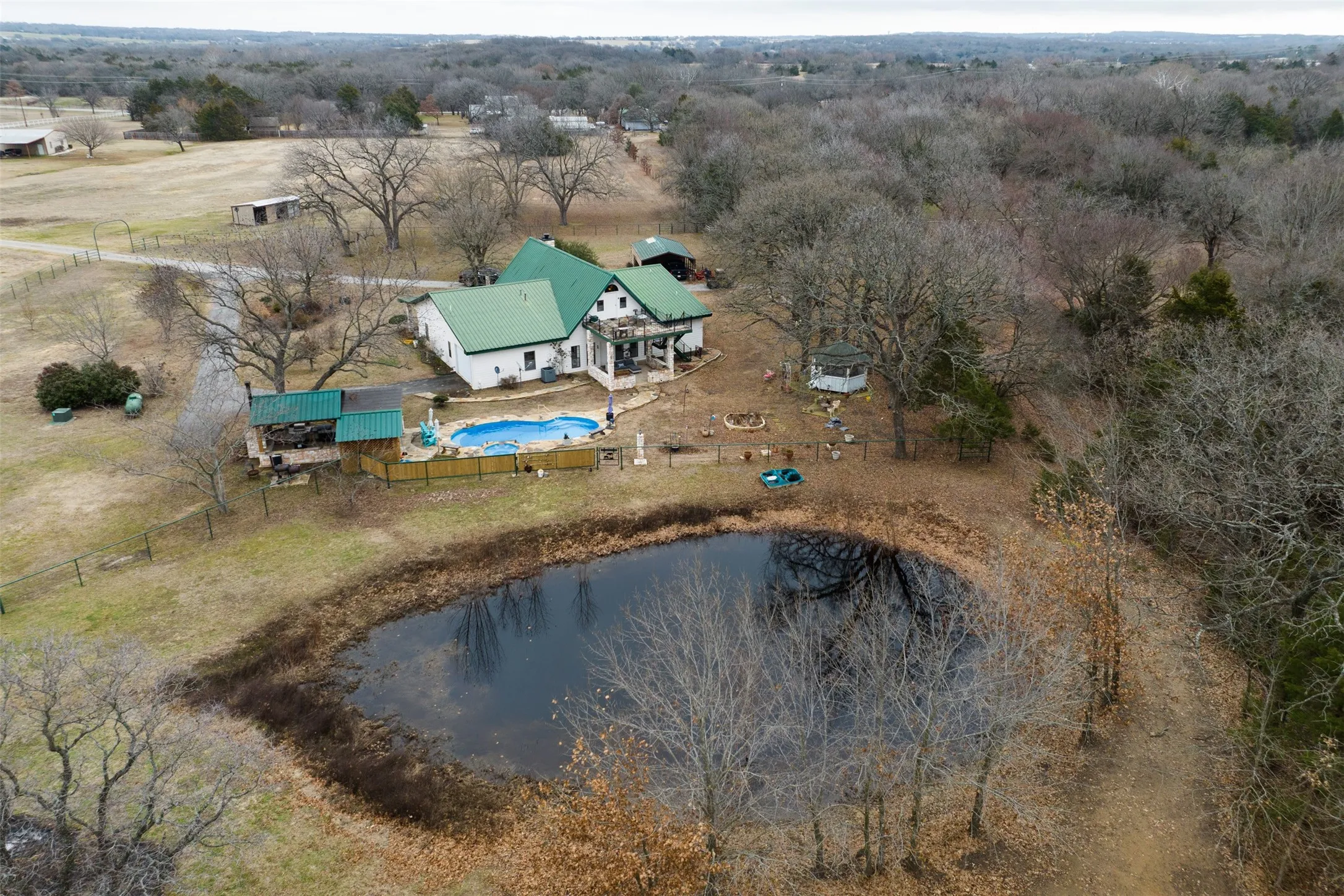 Expansive property featuring a private pond, in-ground swimming pool, and a white residence with a green roof