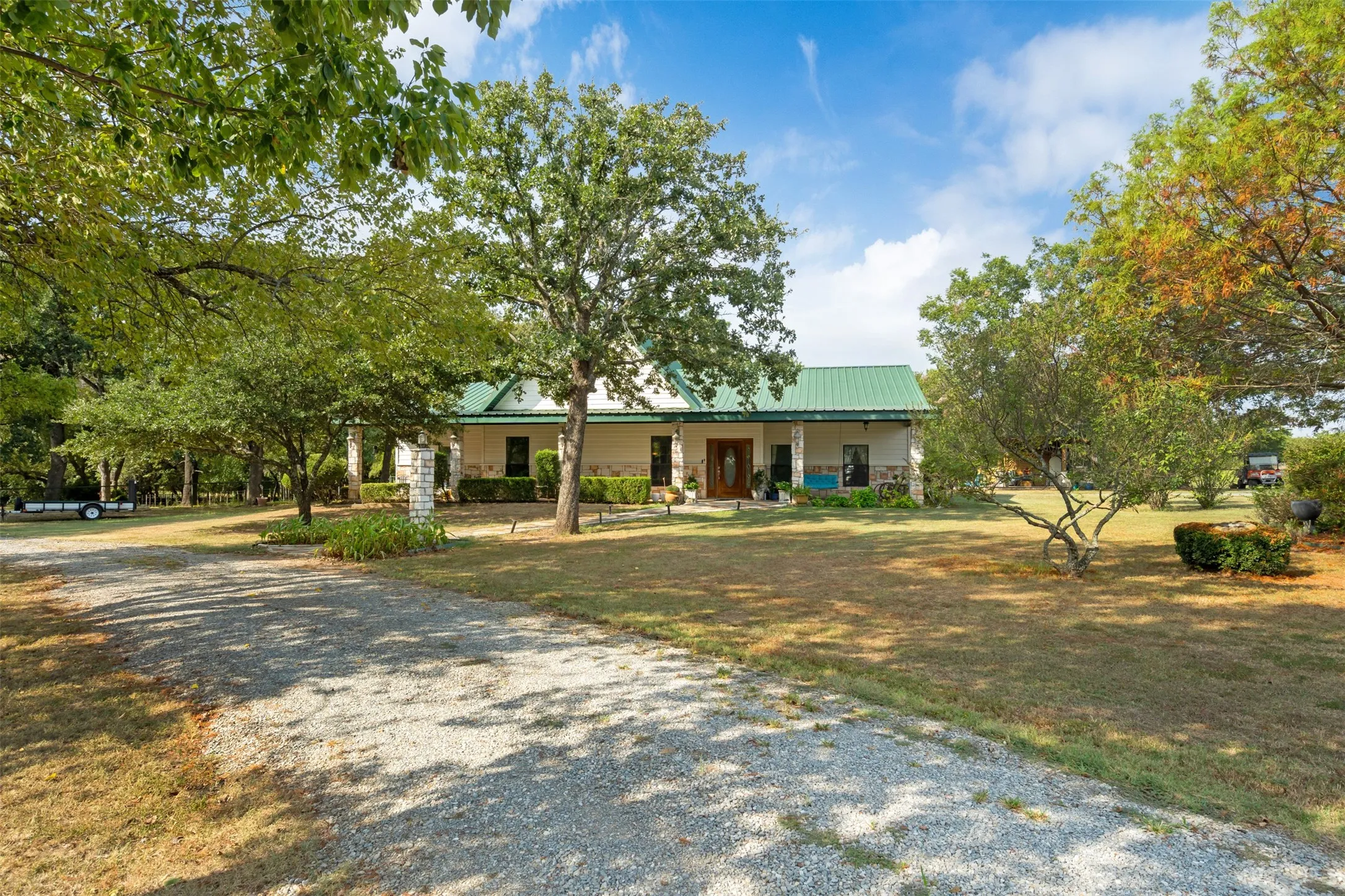 Gravel driveway leading to a residence featuring a green metal roof and stone columns
