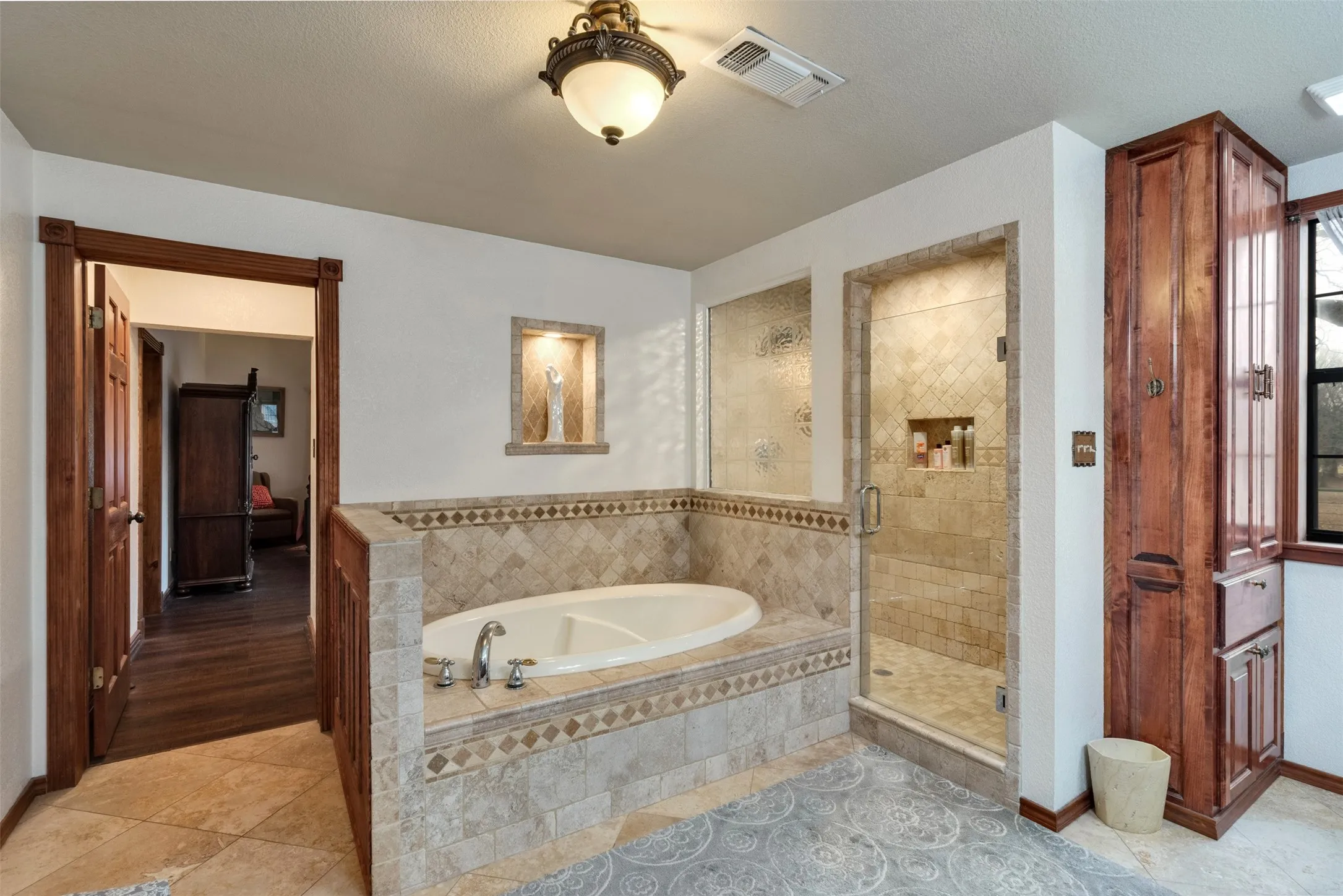 Built-in soaking tub, walk-in shower with glass enclosure, custom wood cabinetry, tiled flooring, and accent wall niche