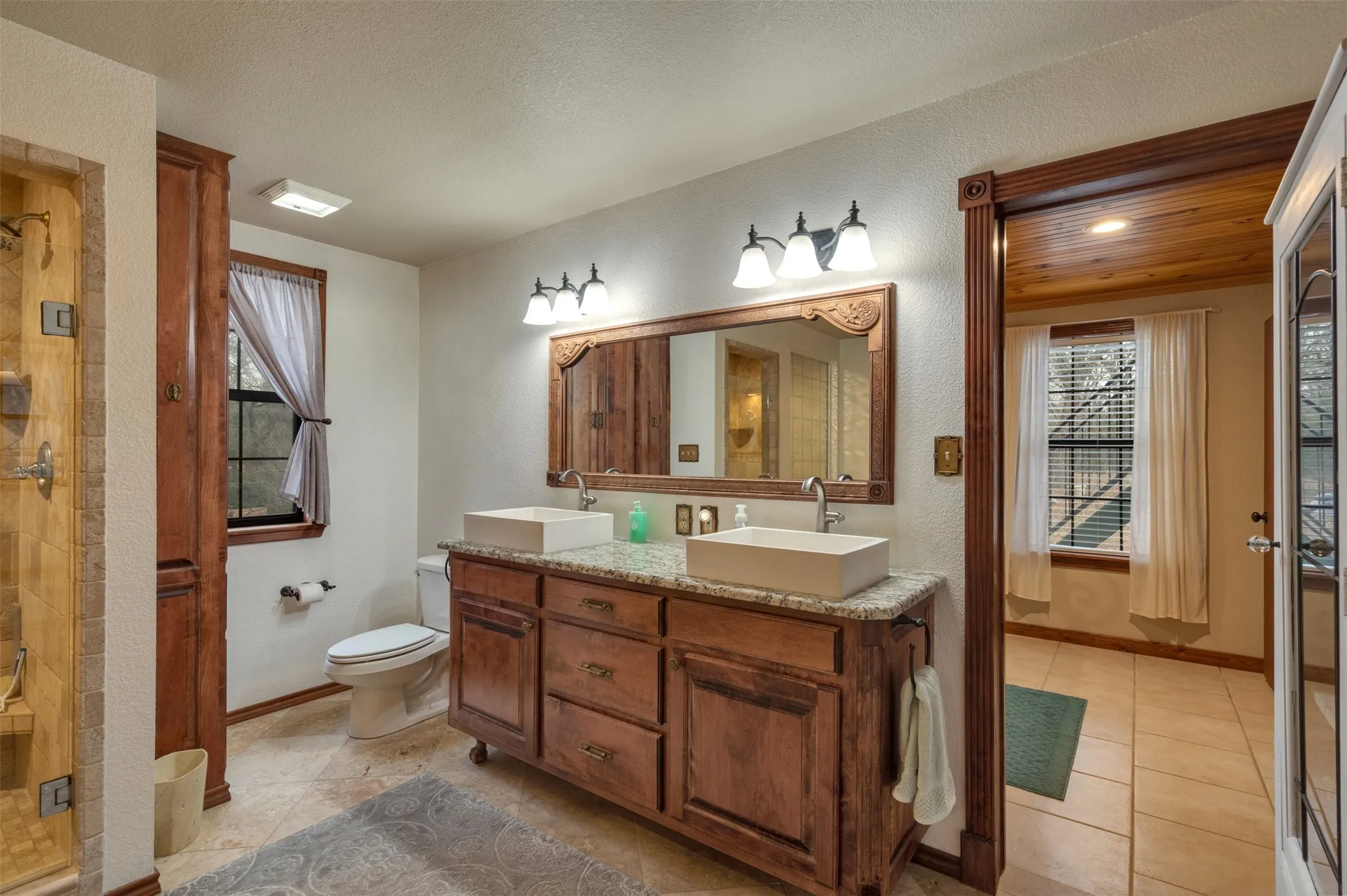 Dual vessel sinks with granite-finish countertop, custom wood vanity, and decorative mirror