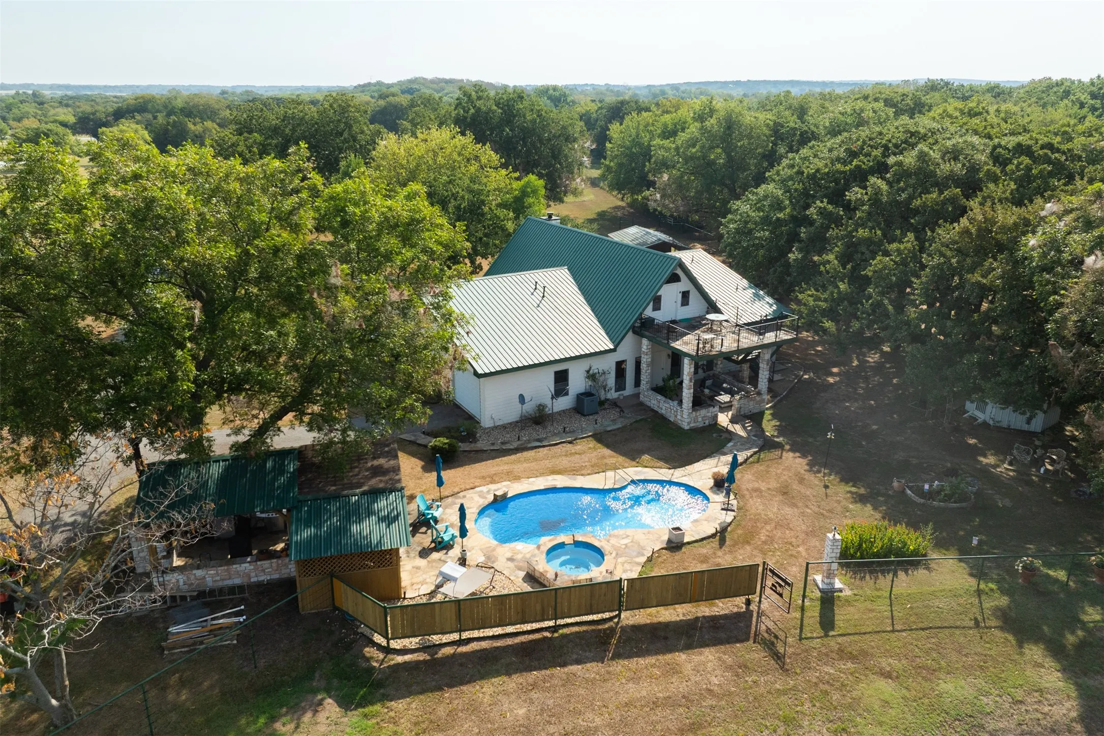 Two-story residence featuring a green metal roof, a stone-paved pool deck with an integrated spa, and a fenced swimming pool
