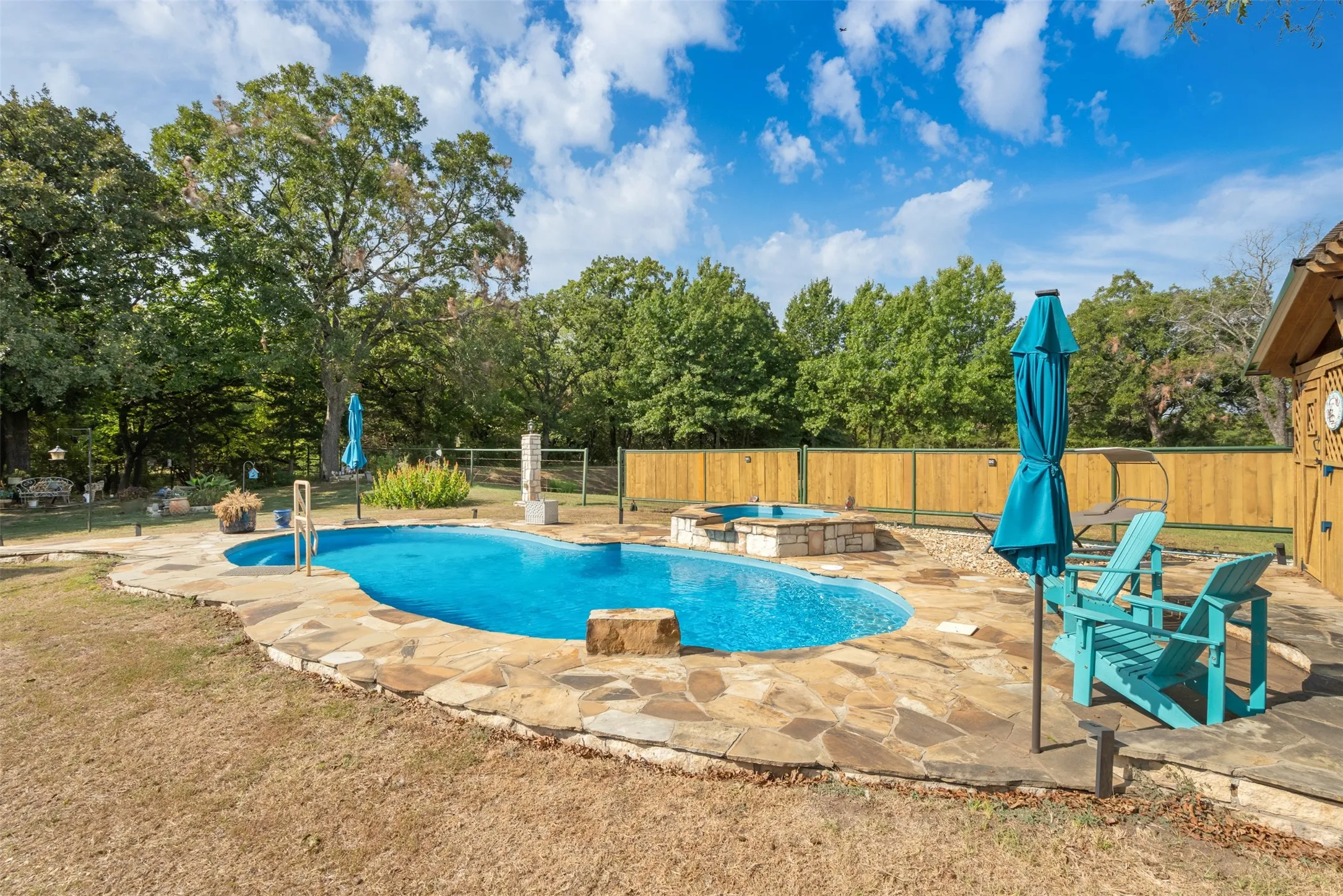 Resort-style backyard featuring a freeform swimming pool, integrated hot tub, flagstone patio, and privacy fencing