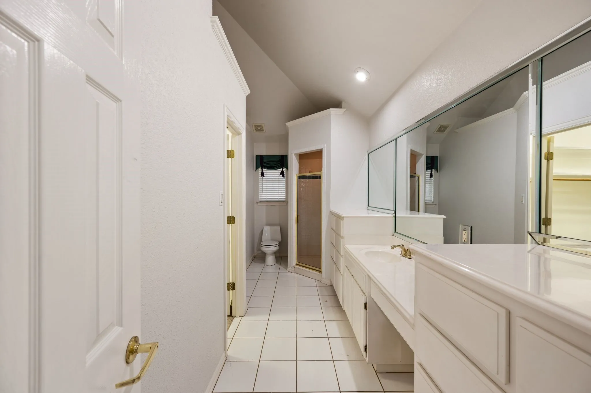 Bathroom featuring a double vanity with integrated sink, expansive mirrored wall, white tile flooring, and a glass-enclosed shower