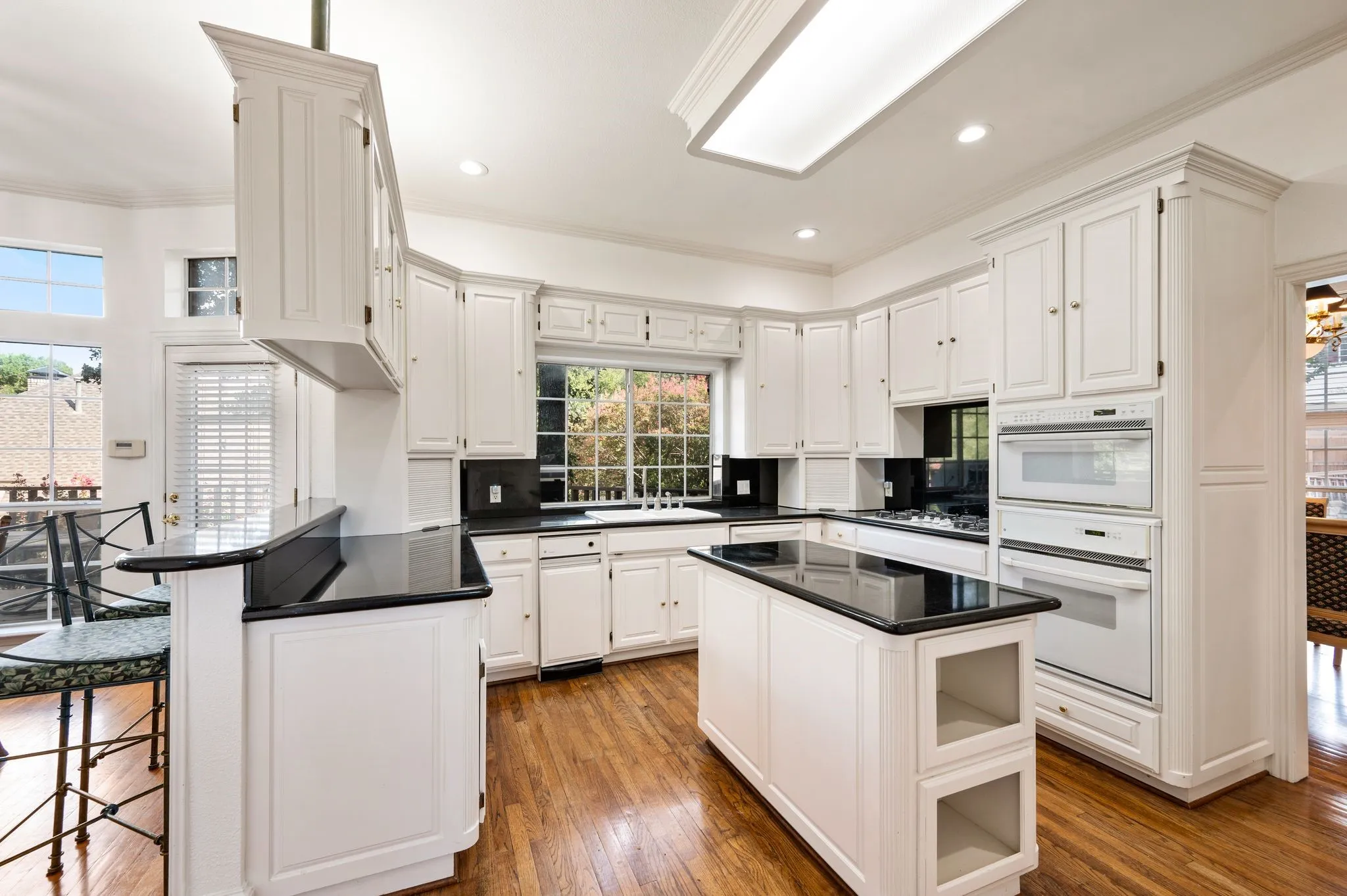 Kitchen featuring white cabinetry, dark countertops, a central island, integrated wall oven and microwave, and wood-finish flooring