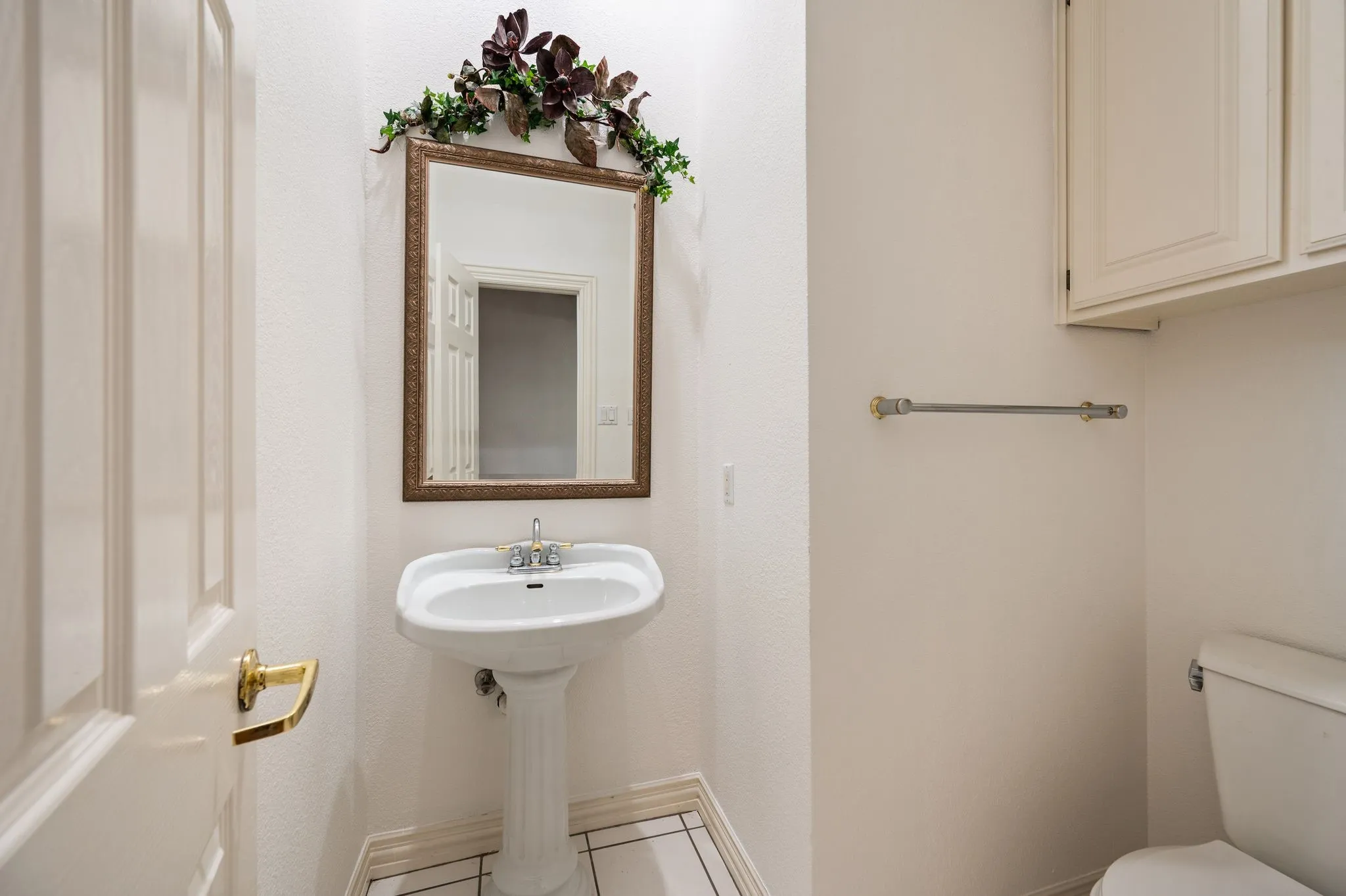 Powder bath with pedestal sink, chrome faucet, framed wall mirror, built-in cabinetry, and tile flooring