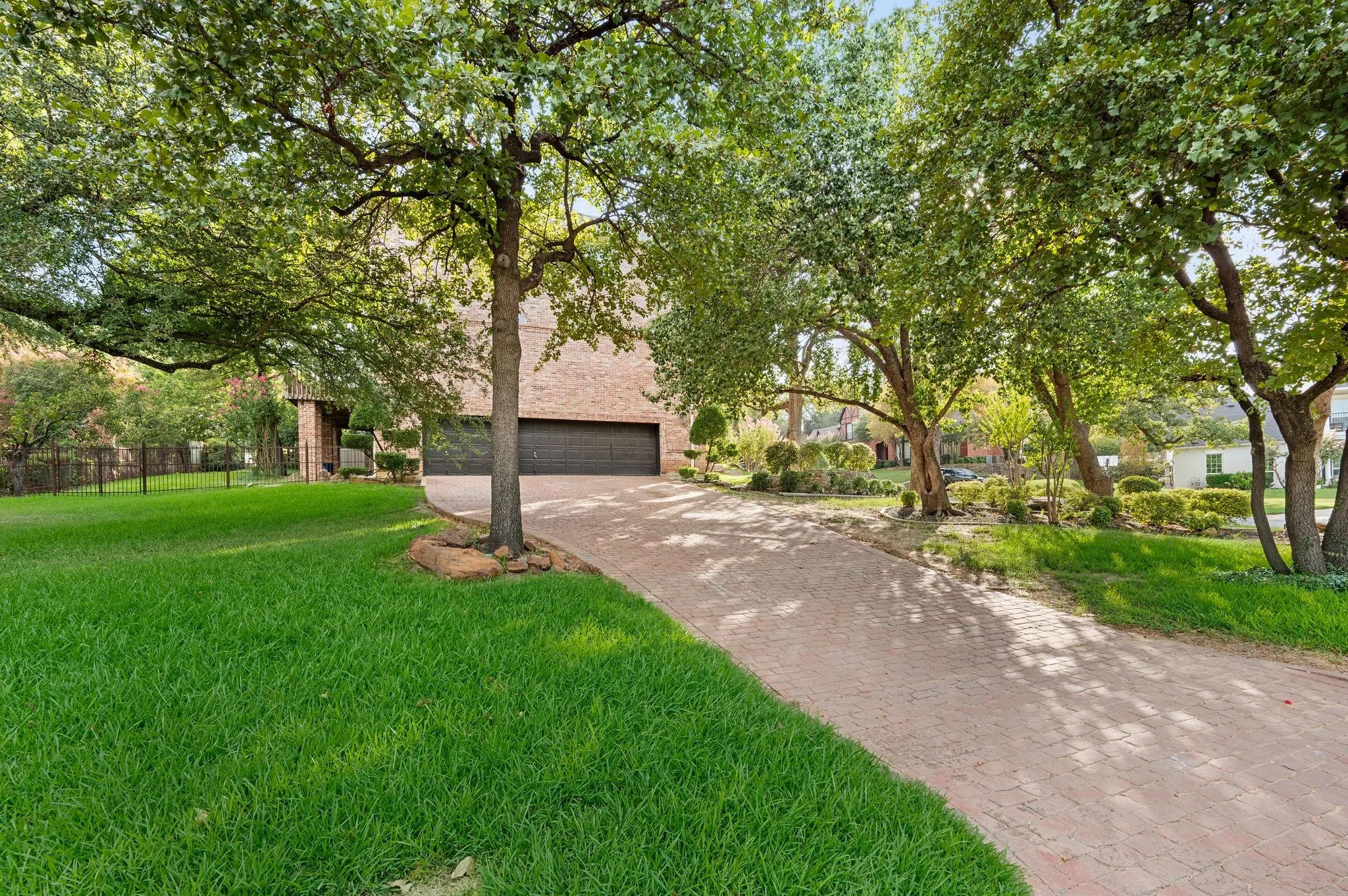 Brick paver driveway, mature trees, green lawn, brick exterior, and attached garage