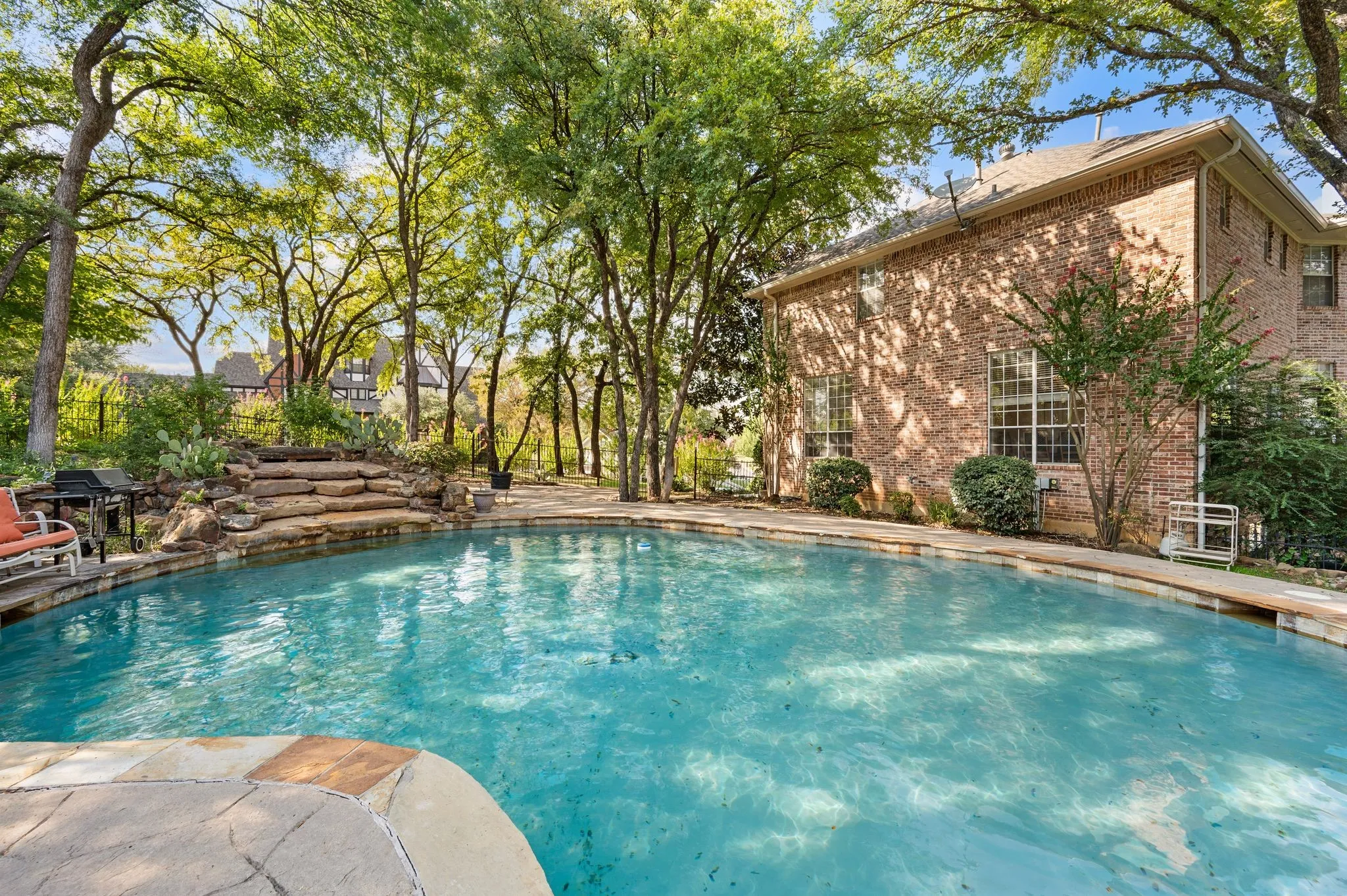 Rectangular pool with integrated stone waterfall feature, surrounded by flagstone coping and mature trees