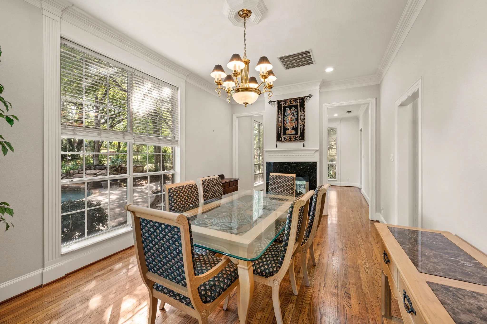 Hardwood flooring, crown molding, large divided light window, decorative fireplace, and a multi-arm chandelier