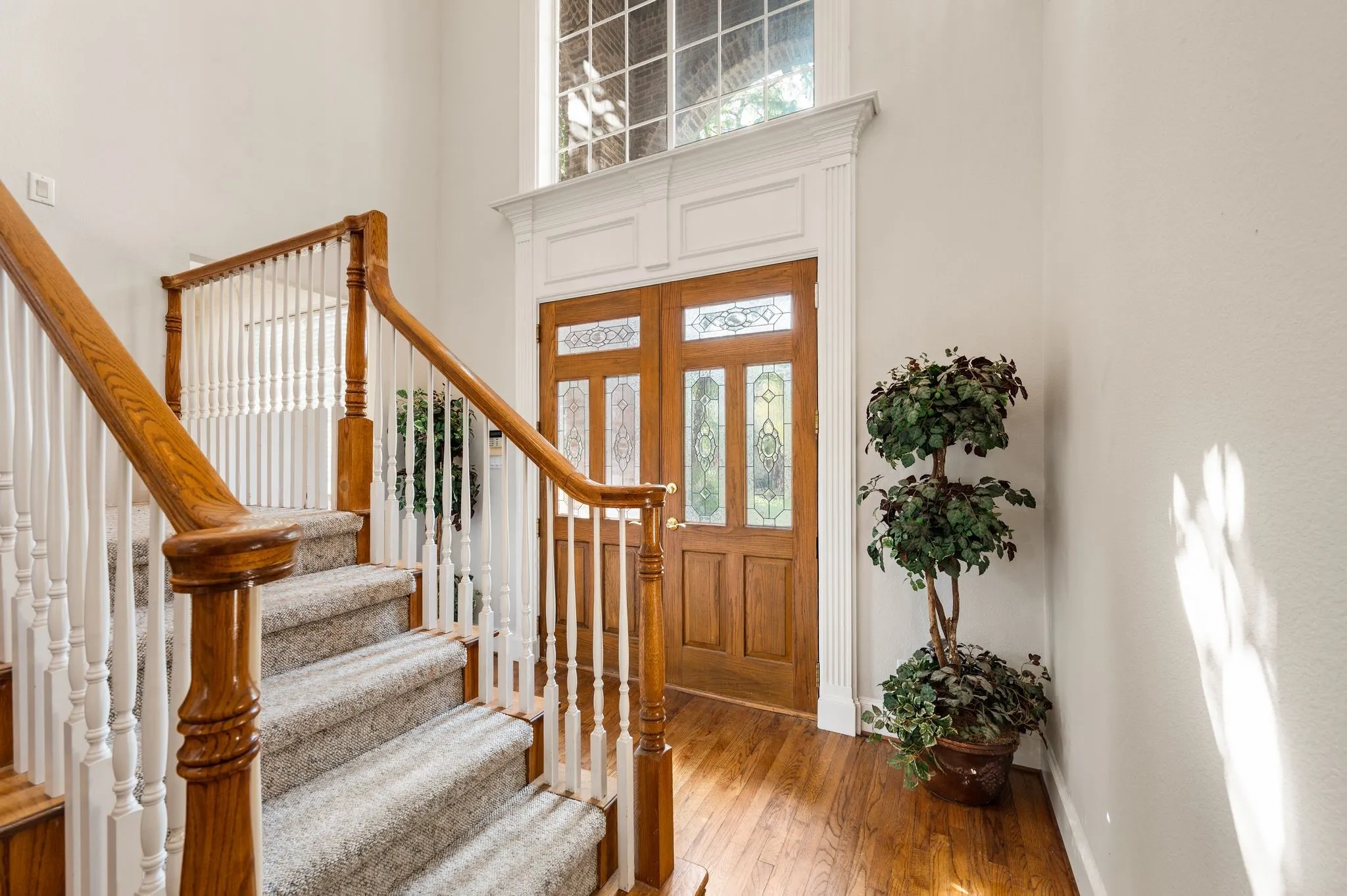 Two-story entryway featuring a wood-finish double door with leaded glass, an arched transom window, and wood-finish flooring