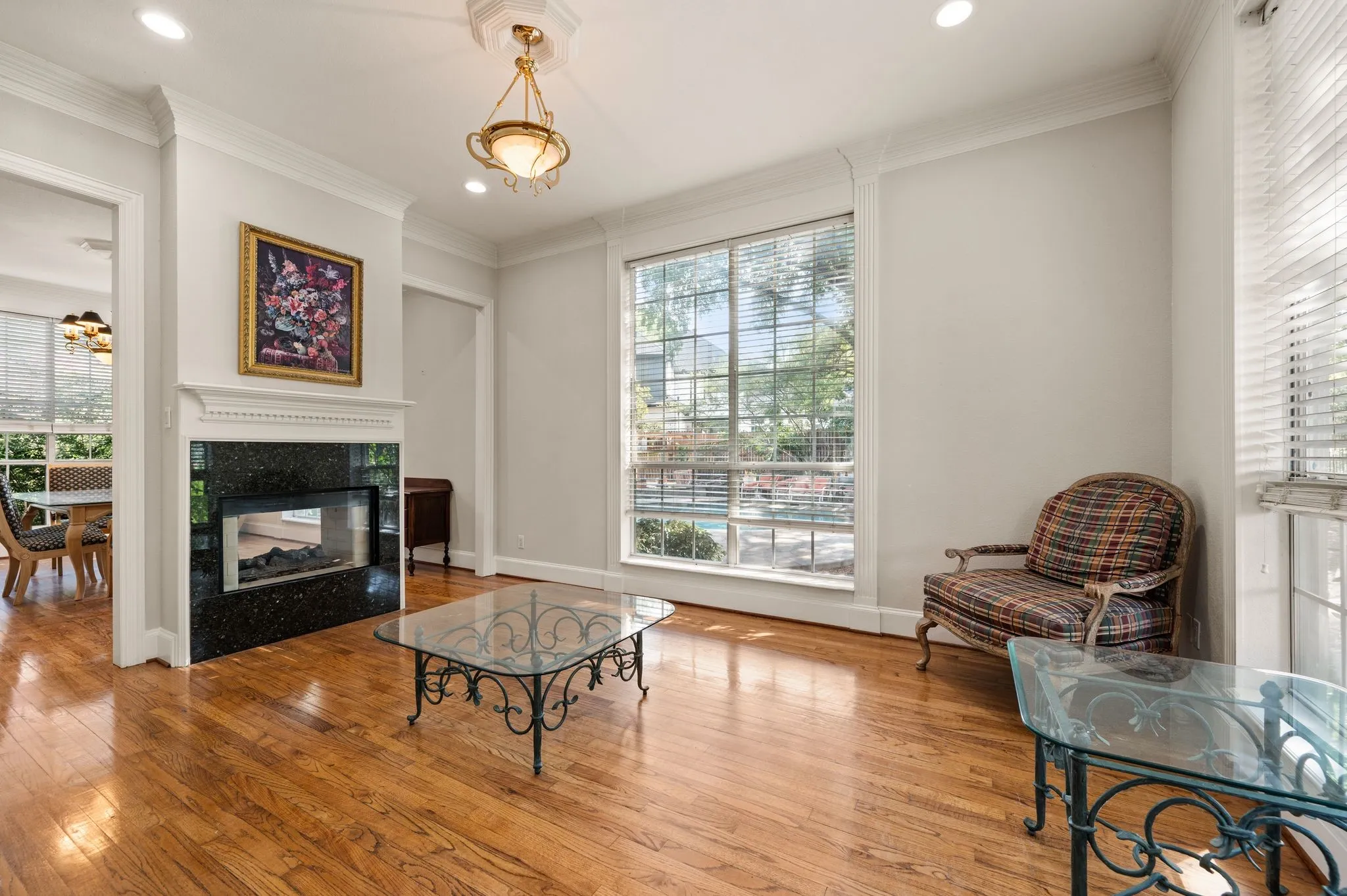 Hardwood flooring, recessed lighting, crown molding, fireplace with dark stone surround, and a large window