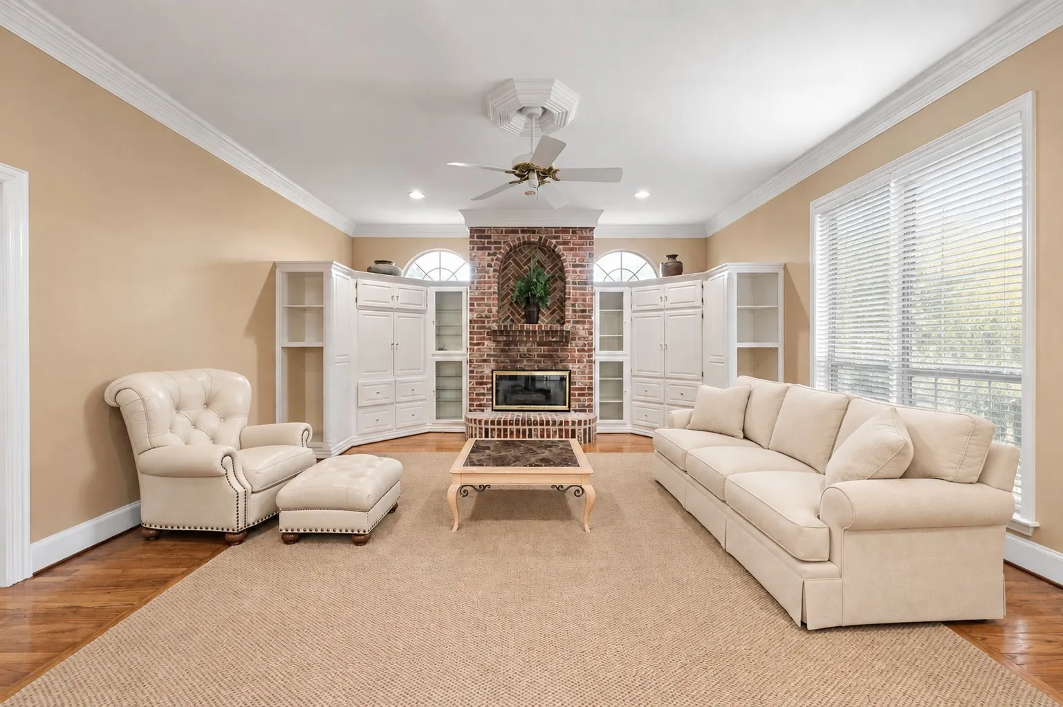 *Virtually edited* Brick fireplace with arch accents, built-in cabinetry, crown molding, wood-finish flooring, and a ceiling fan with light fixture