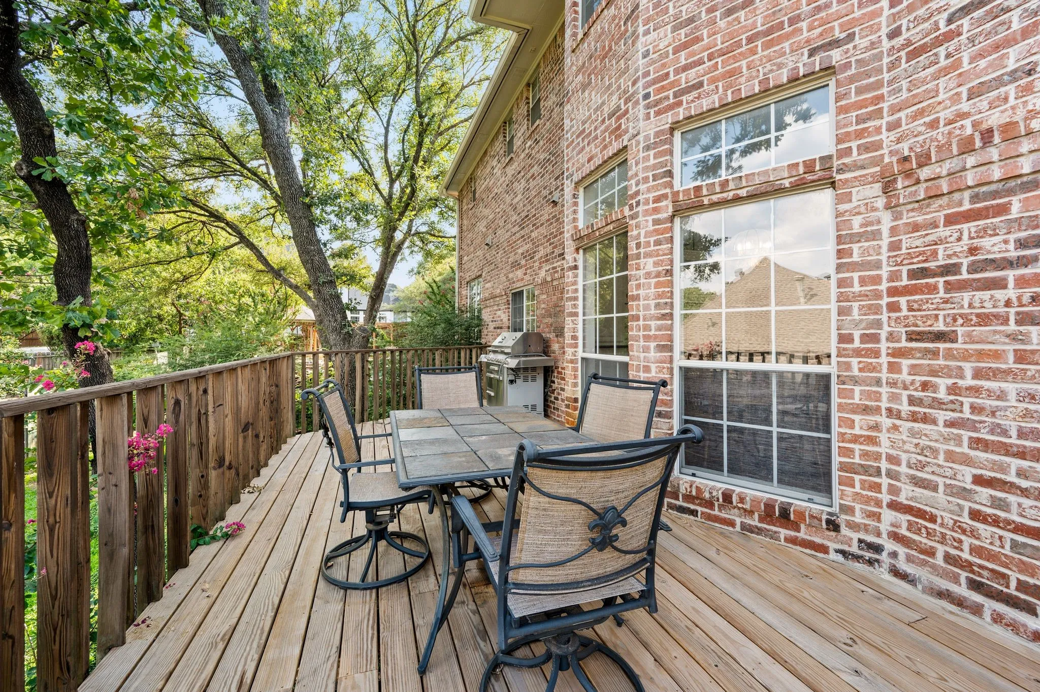 Expansive outdoor wood deck with natural wood railing, set against a brick exterior with multiple windows