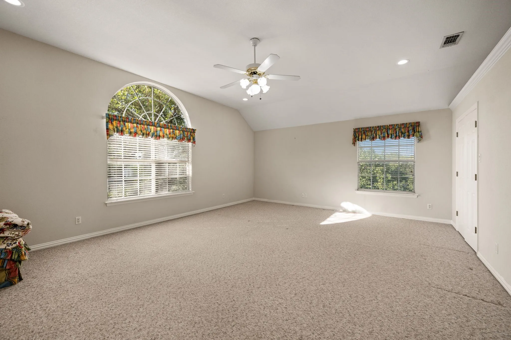 Spacious room featuring vaulted ceilings, carpet flooring, multiple windows with blinds, a large arched window, and a ceiling fan with integrated lighting