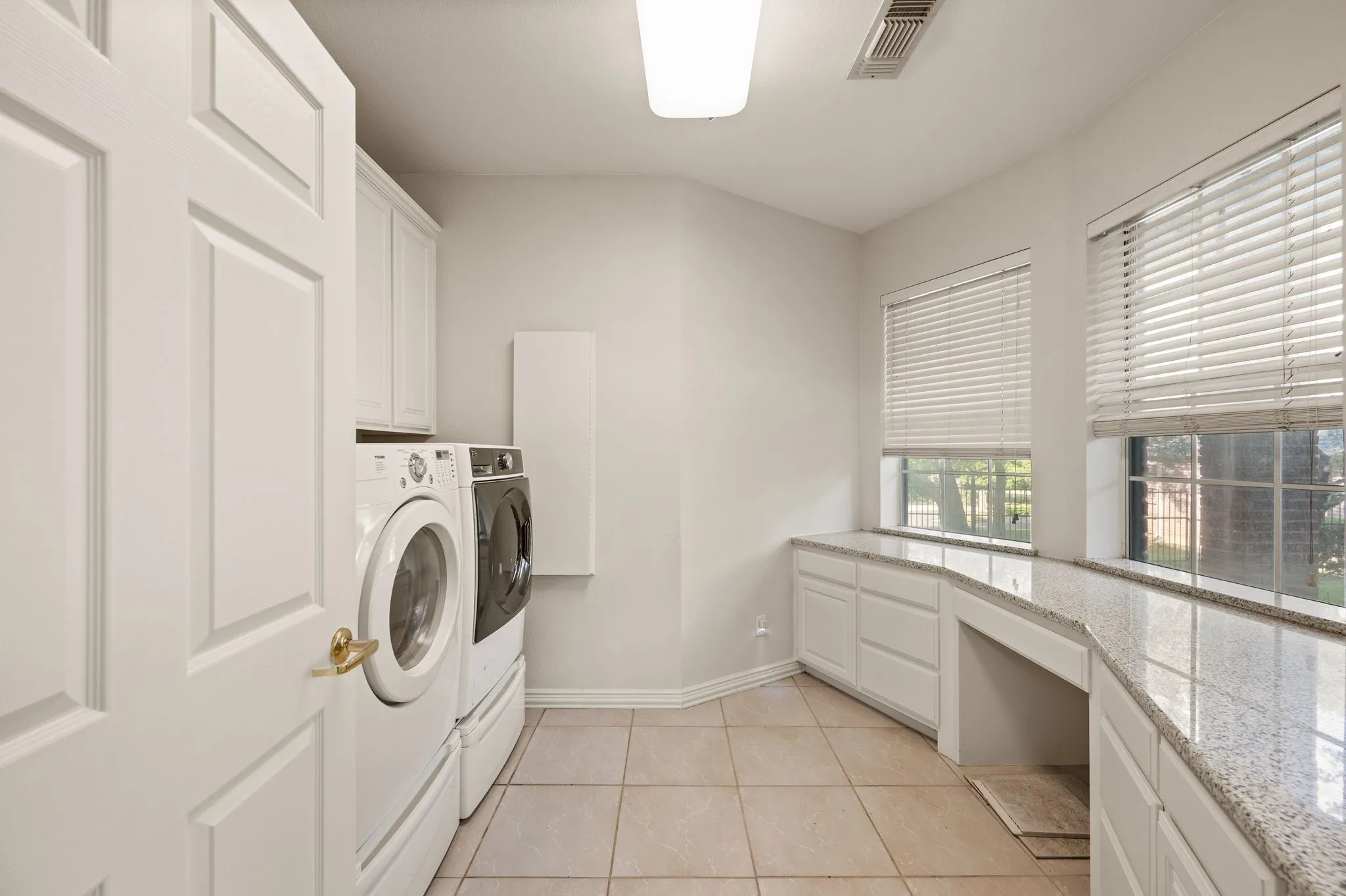 Laundry room featuring tile flooring, built-in white cabinetry, light-toned countertop, and multiple windows