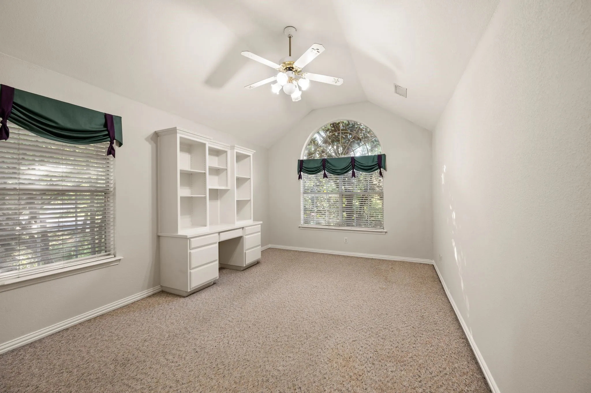 Vaulted ceiling with a ceiling fan, built-in desk with shelving, and an arched window