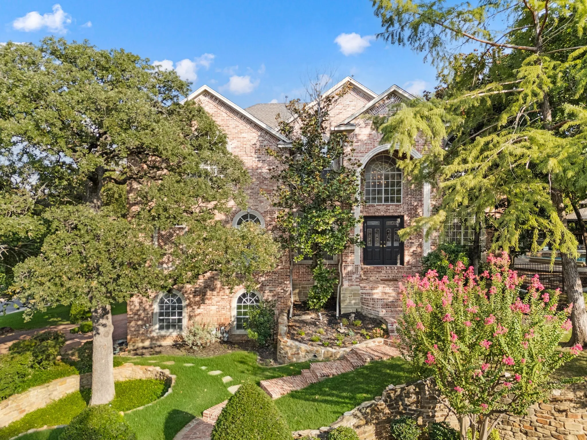 Brick exterior with arched windows, mature landscaping, and a grand entry with double doors