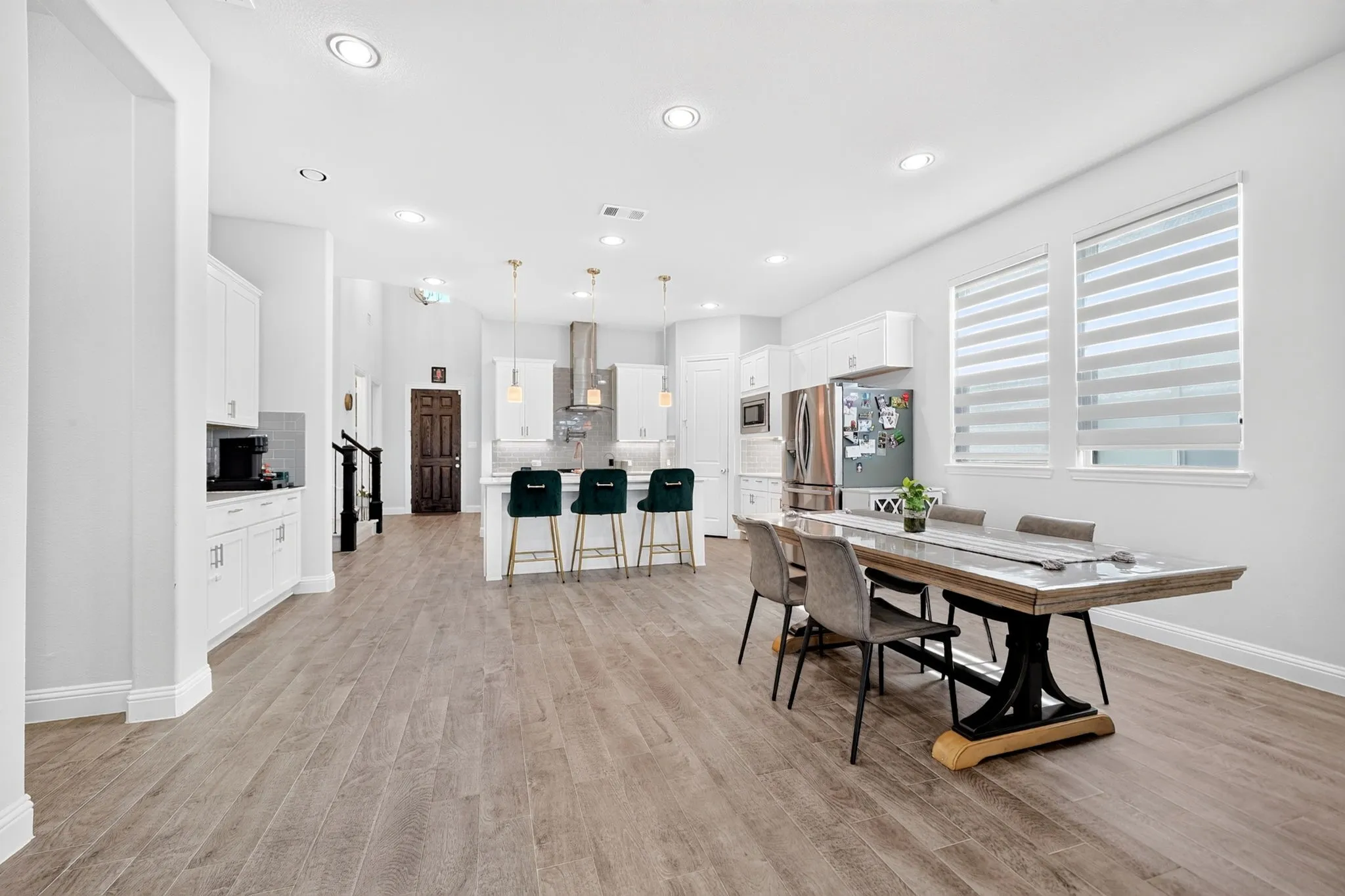 Wood-finish flooring throughout, recessed lighting, white cabinetry, stainless steel appliances, and large windows with blinds