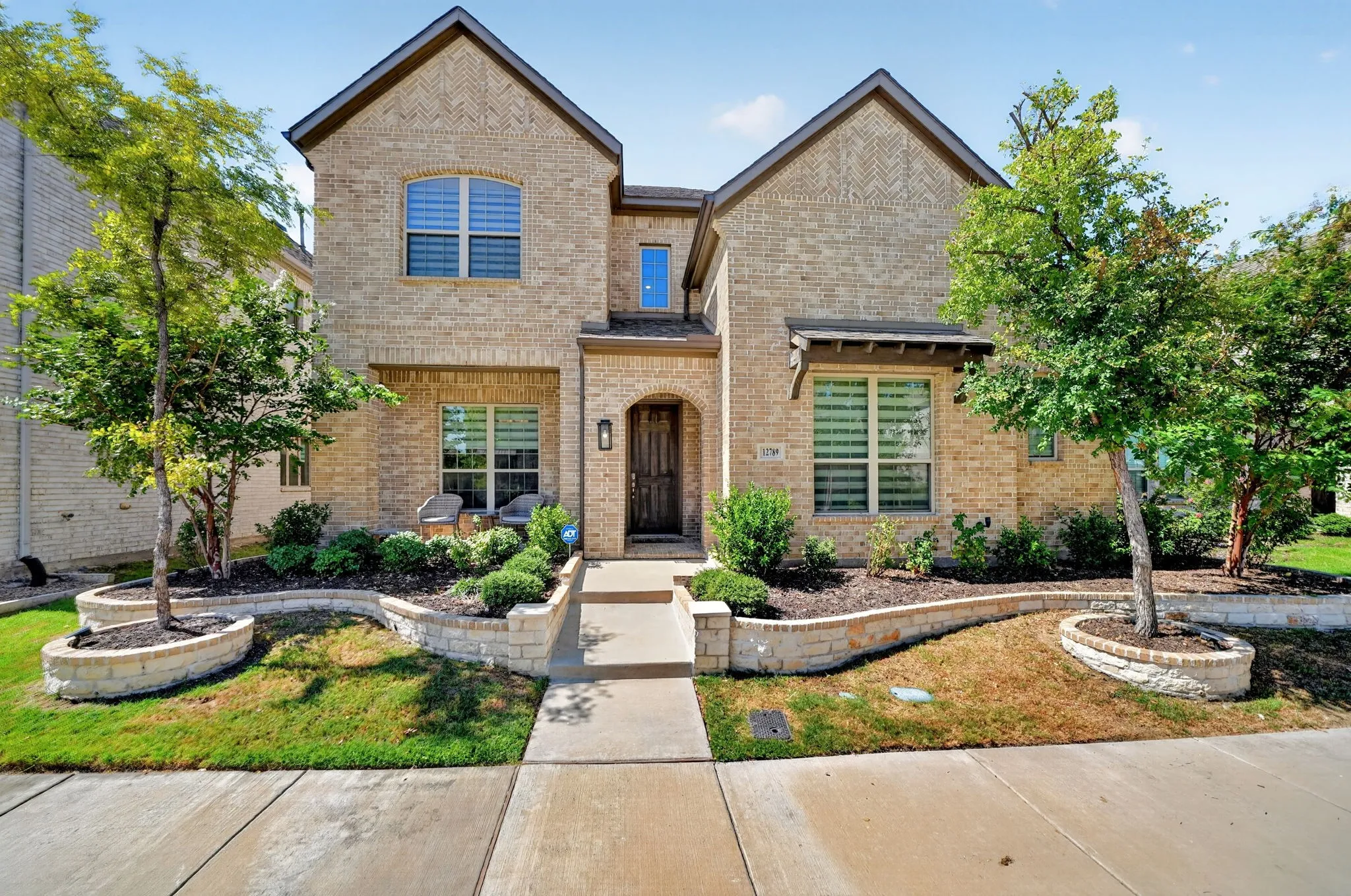 Light brick facade, gabled roofline, arched entry, stone-clad planter beds, and mature landscaping