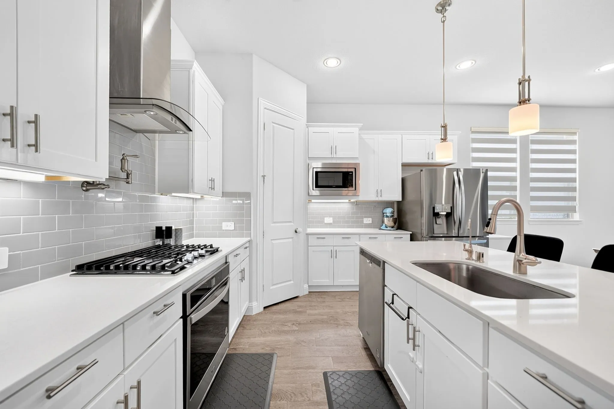 White shaker cabinetry, light-toned countertops, subway tile backsplash, stainless steel appliances, and an island with an undermount sink