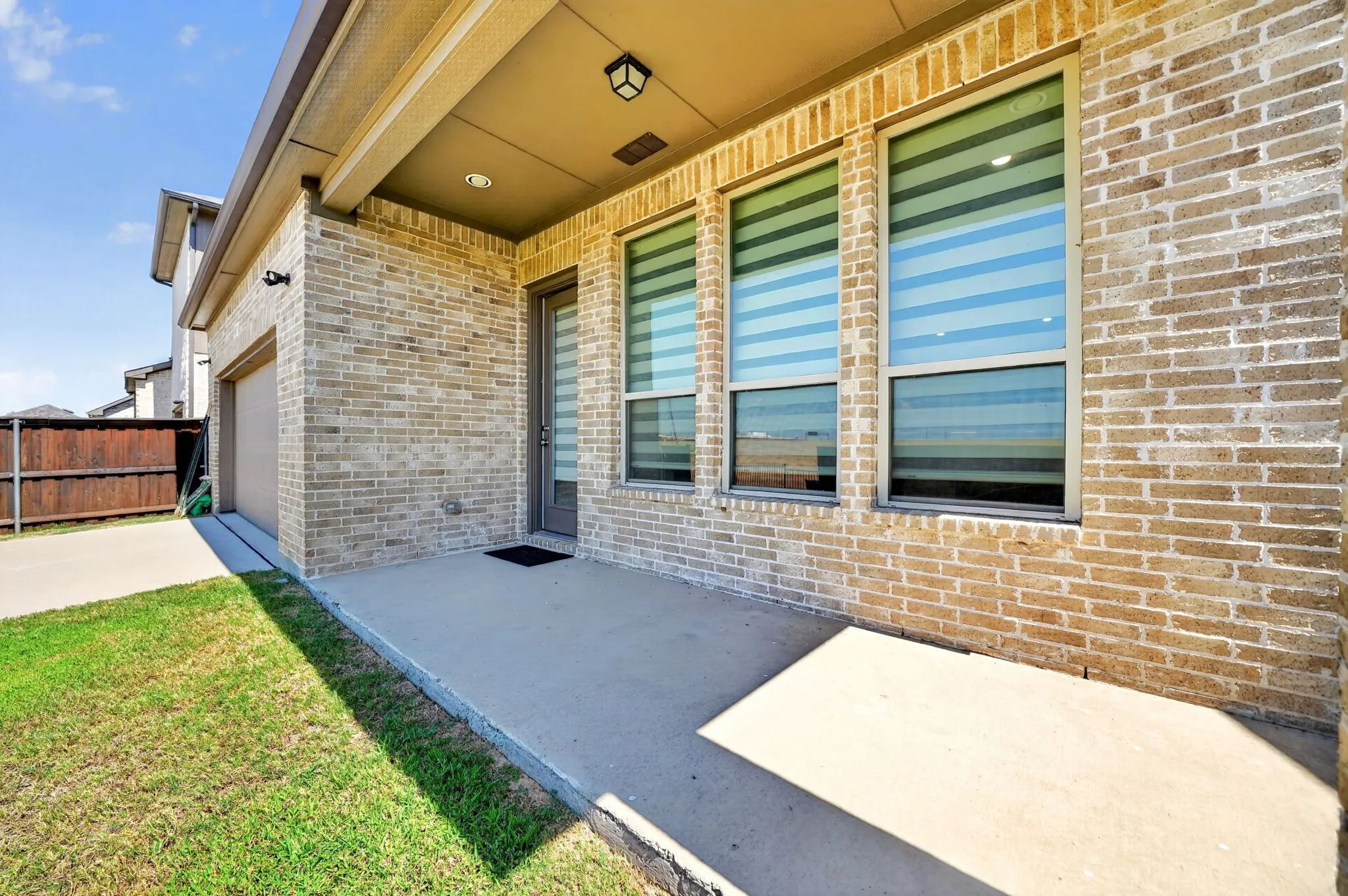 Brick exterior with a covered patio, three large windows, a side-entry garage, and a wood privacy fence