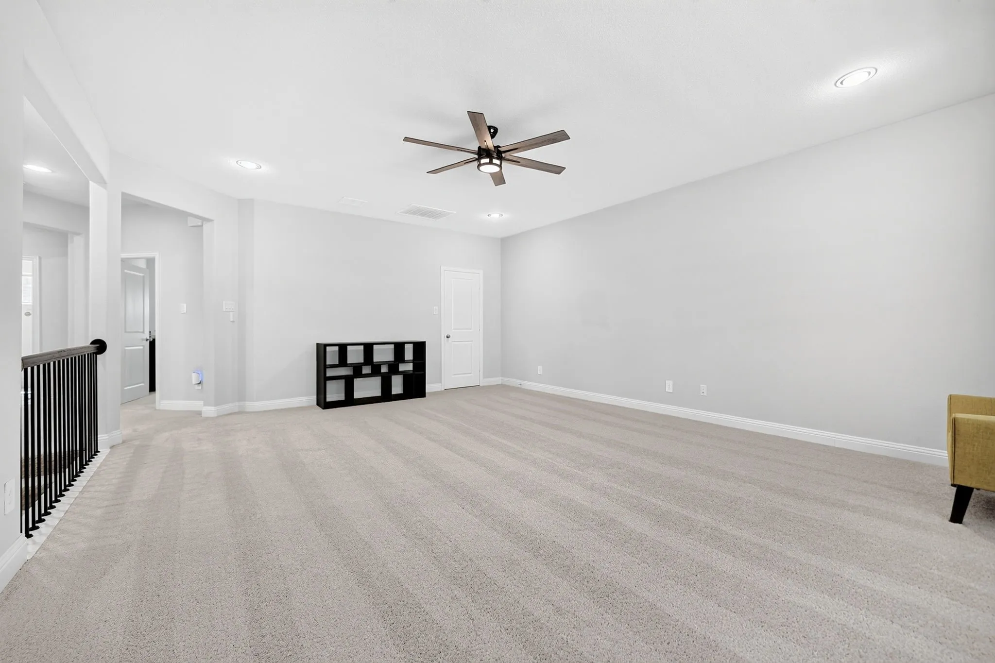 Expansive carpeted area with a ceiling fan and recessed lighting, featuring a white paneled door
