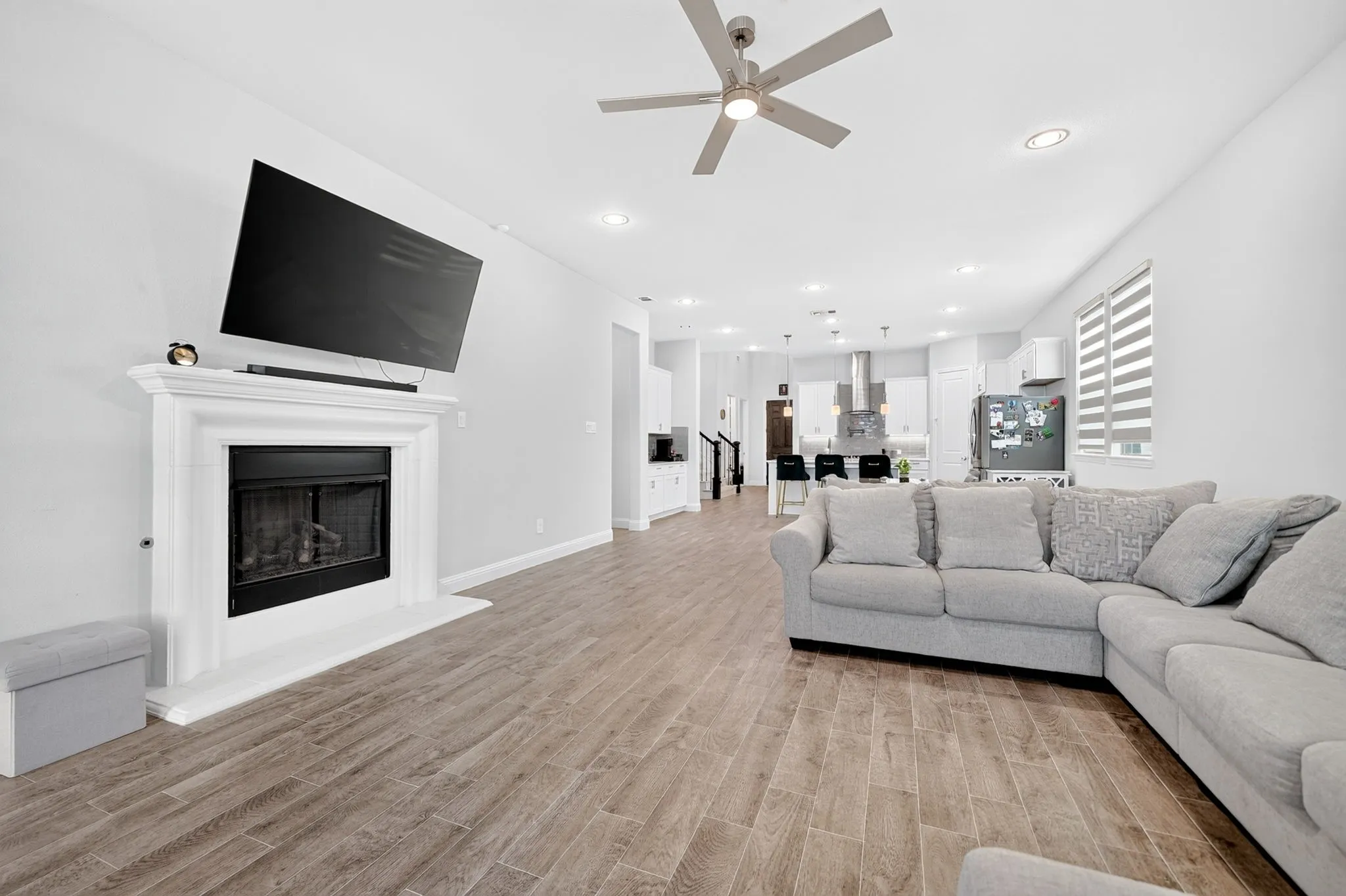Fireplace with a classic white mantel, wood-finish flooring, recessed lighting, and a ceiling fan