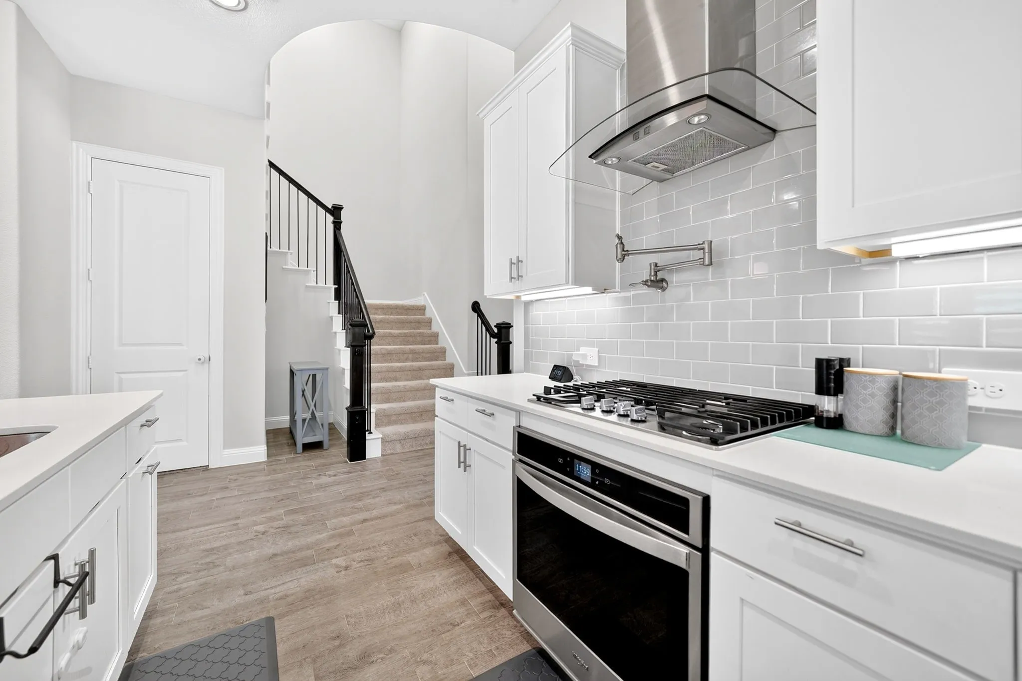 Modern kitchen featuring white cabinetry, stainless steel oven and gas cooktop, light grey subway tile backsplash, and light-toned wood-finish flooring