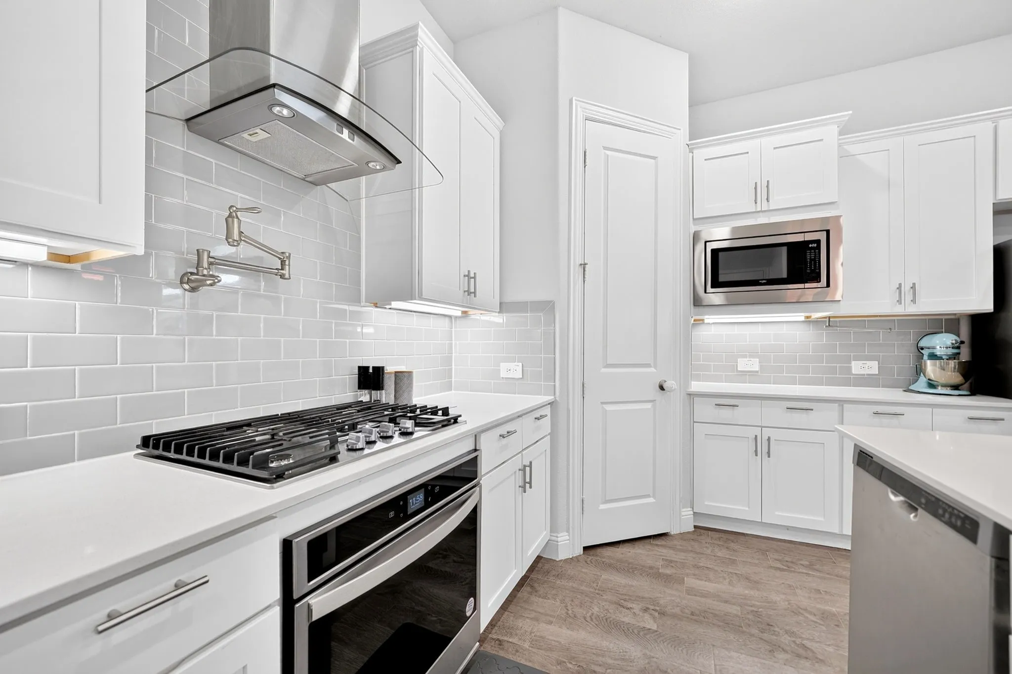 White shaker cabinetry, light-toned subway tile backsplash, stainless steel appliances, solid surface countertops, and wood-finish flooring