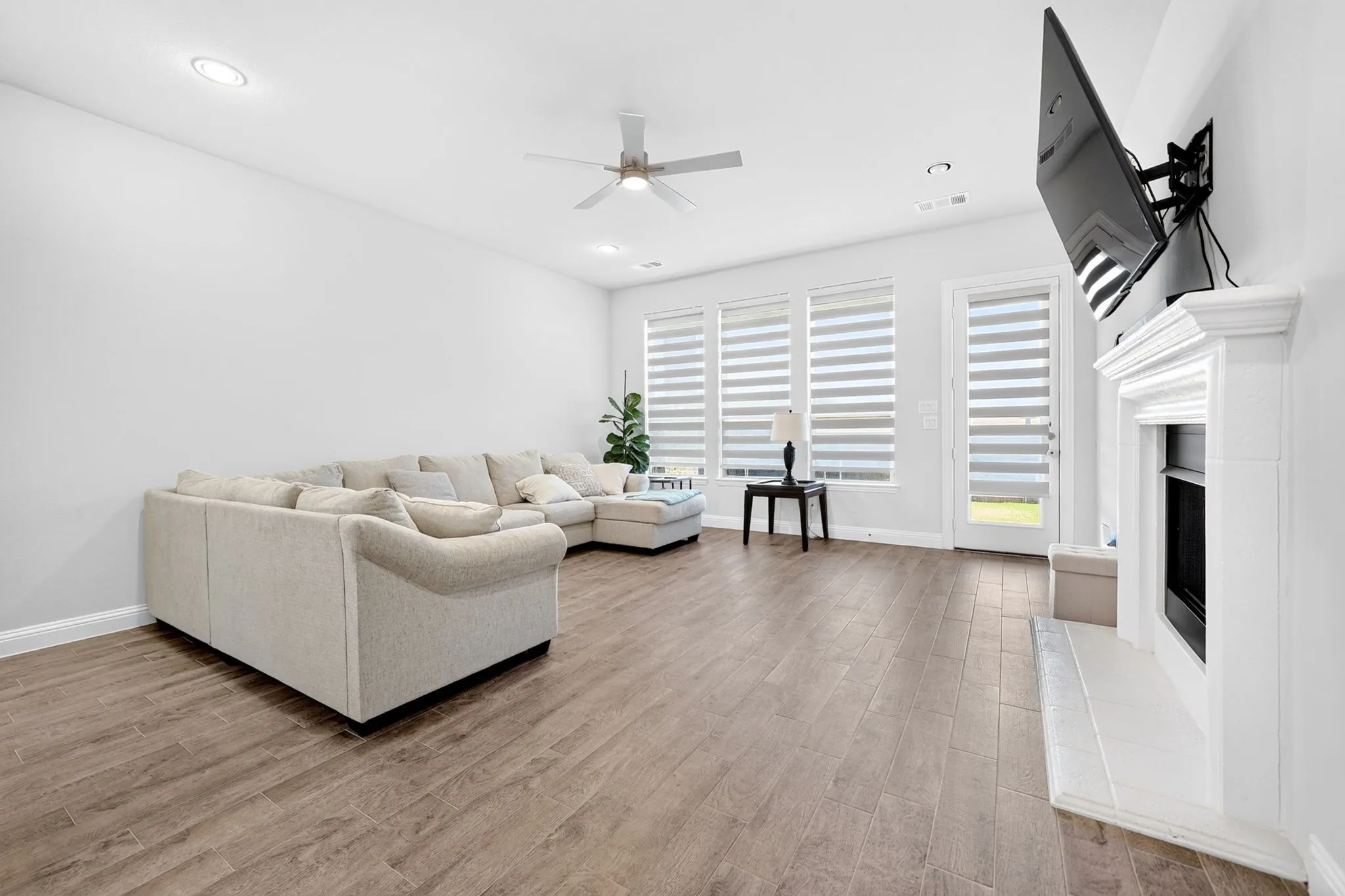 Recessed lighting, wood-finish flooring, ceiling fan, white fireplace, and multiple windows