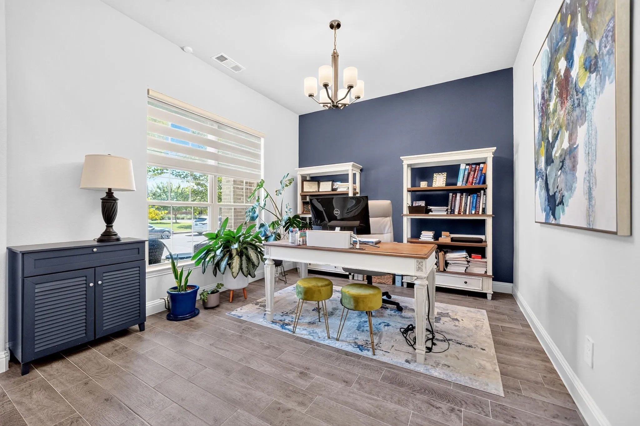 Wood-finish flooring, accent wall, window with blinds, and ceiling-mounted chandelier