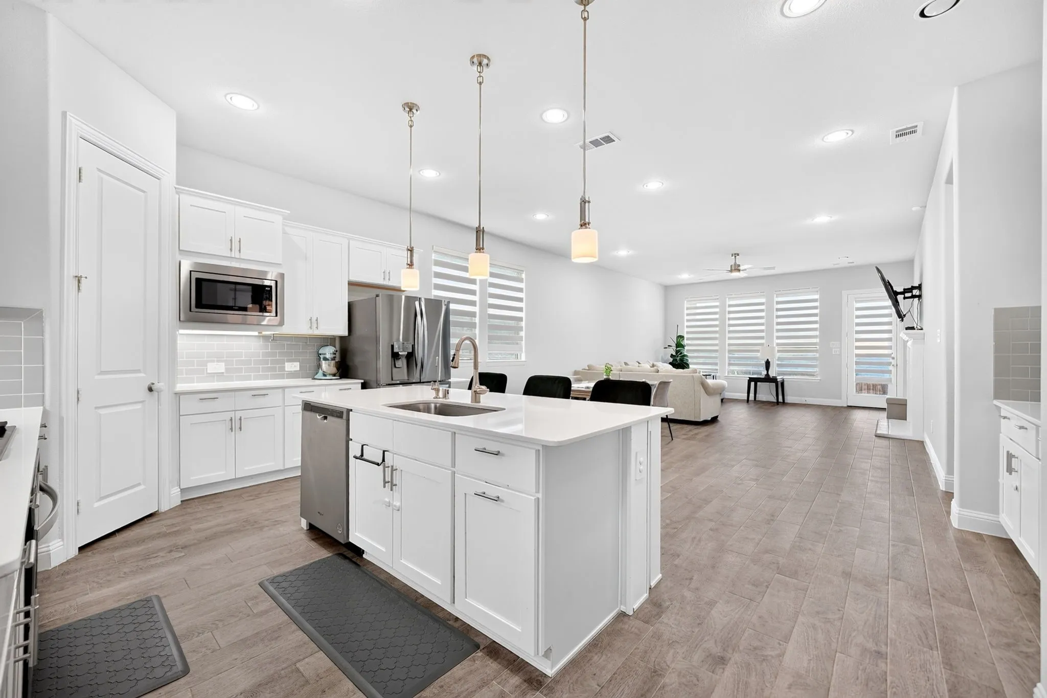 Kitchen featuring white cabinetry, stainless steel appliances, a center island with a sink, pendant lighting, and wood-finish flooring extending into a spacious area
