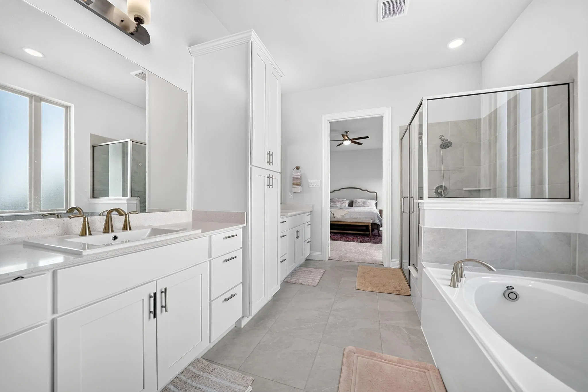 Dual vanity with undermount sinks and brass-finish fixtures, white cabinetry, quartz countertops, soaking tub, and glass-enclosed shower