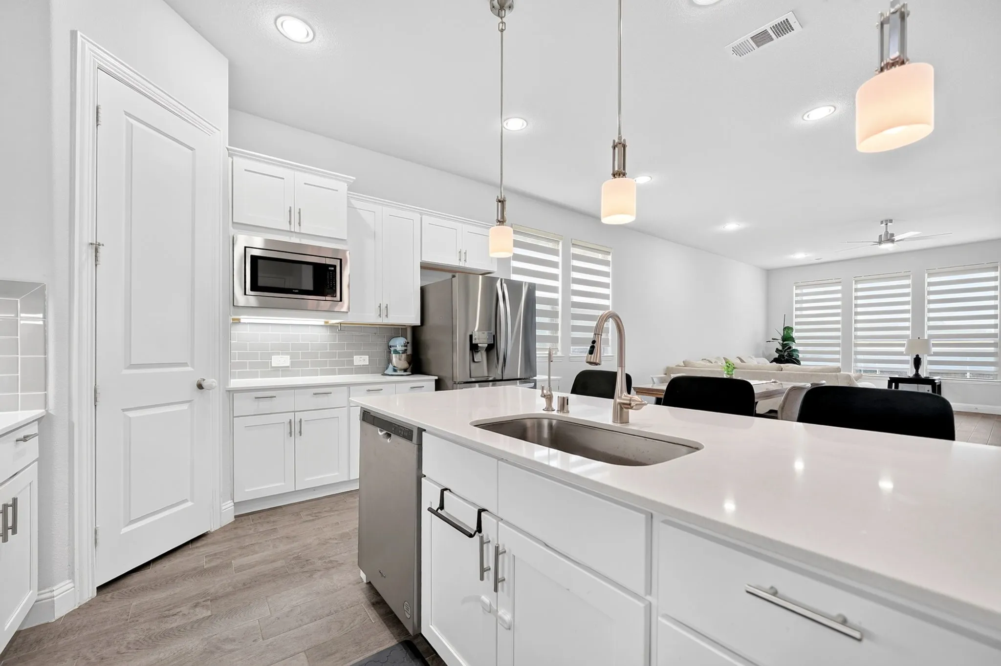 White shaker cabinetry, stainless steel appliances, light subway tile backsplash, white countertop, and wood-finish flooring
