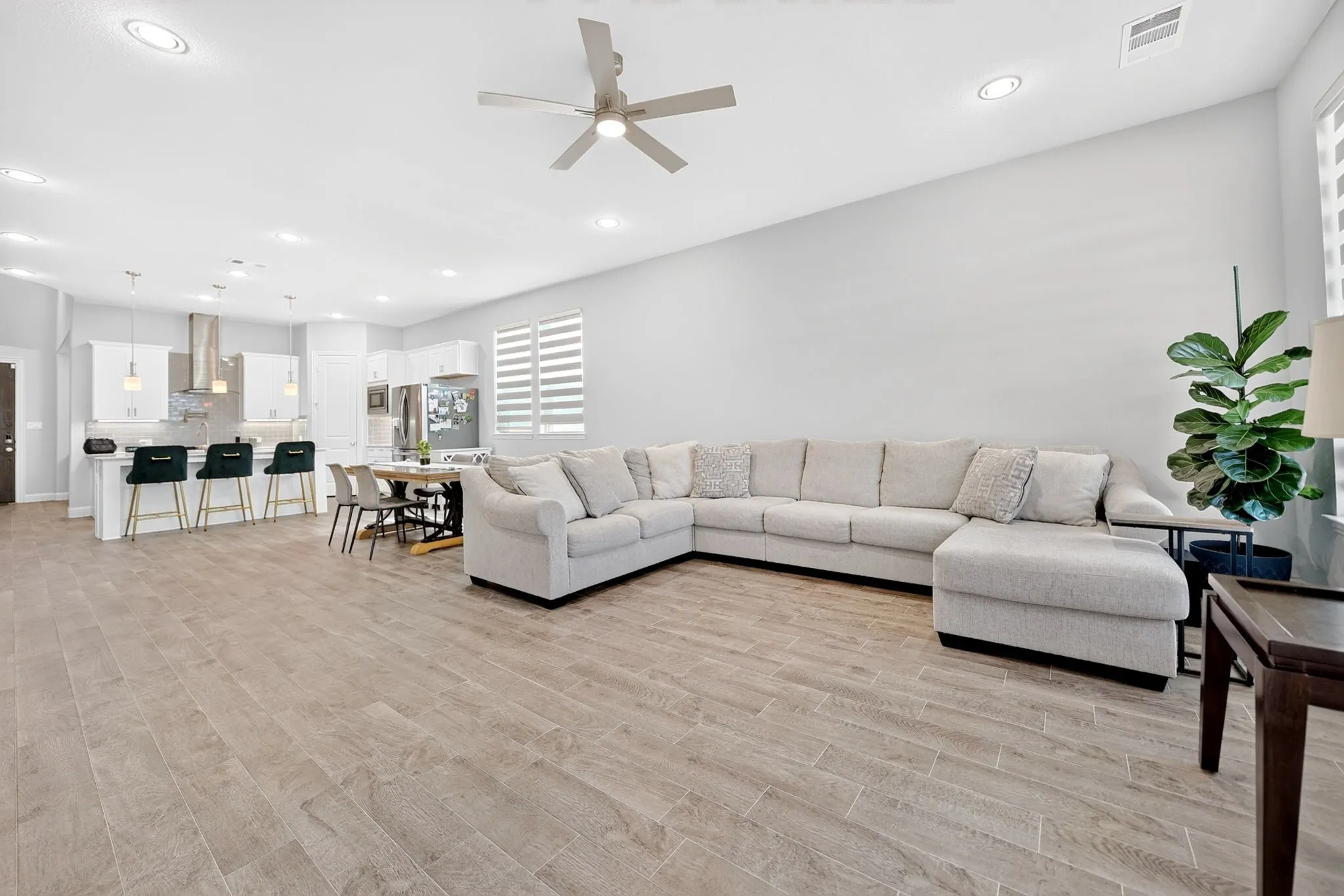 Expansive open-concept living area featuring a curved sectional arrangement, wood-finish plank flooring throughout, recessed ceiling lighting, and a ceiling fan