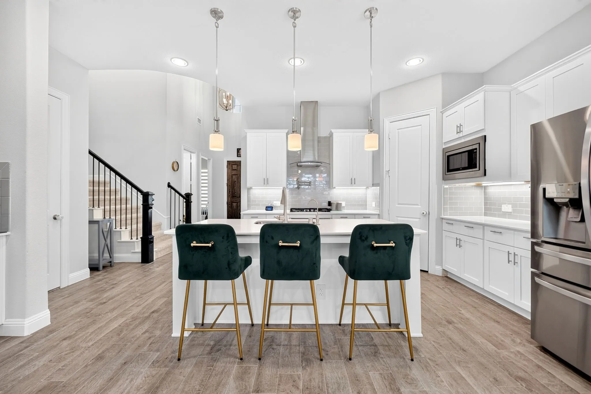 Kitchen featuring a large island, stainless steel appliances, wood-finish flooring, white cabinetry, and a staircase with black railings