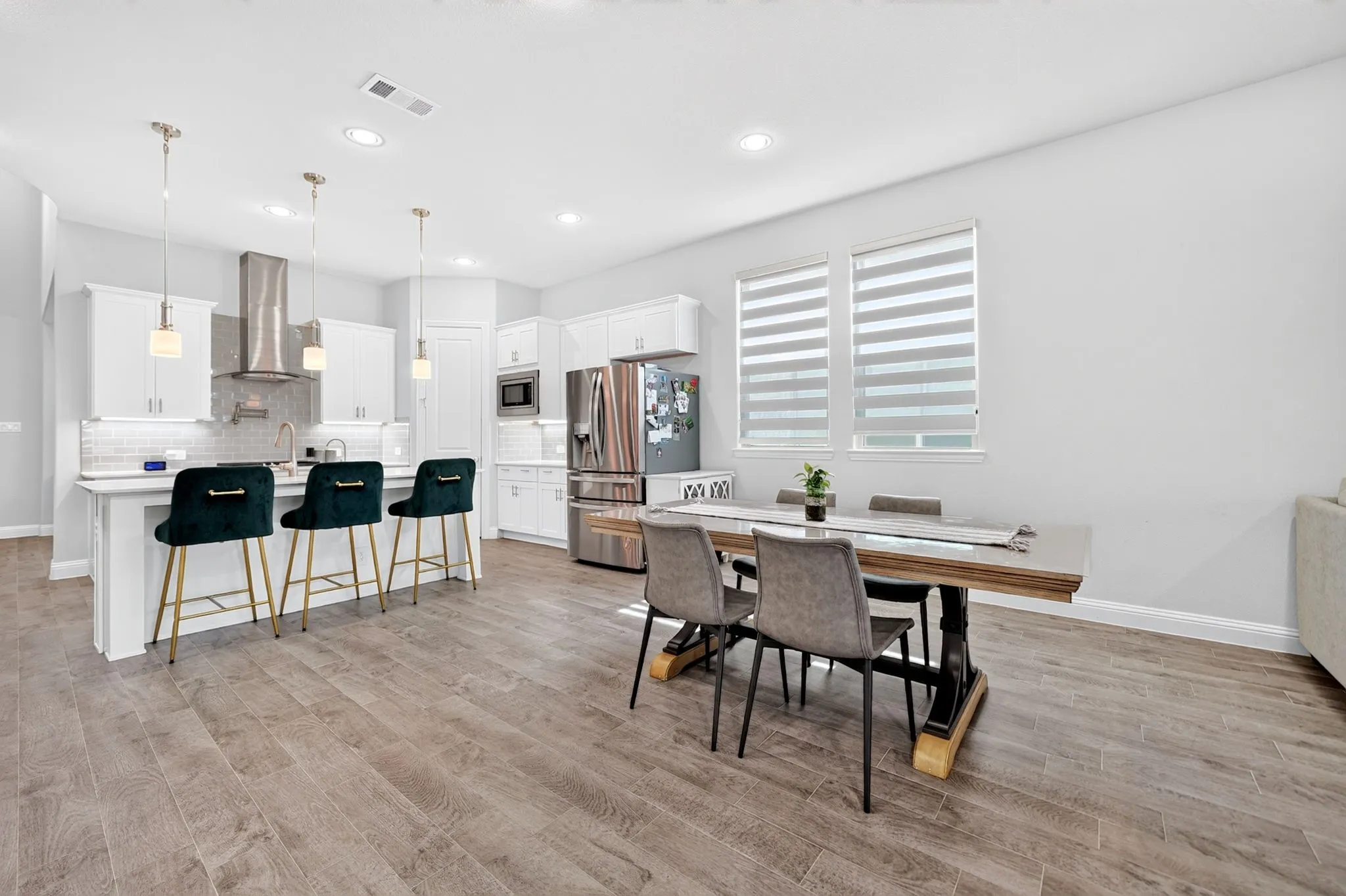 Open-concept layout featuring wood-finish flooring, white cabinetry, a kitchen island with pendant lighting, and stainless steel appliances