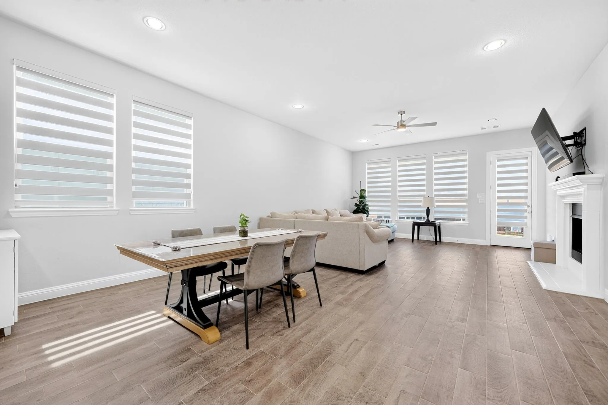 Open-concept living space with wood-finish flooring, a contemporary fireplace, and multiple windows with blinds