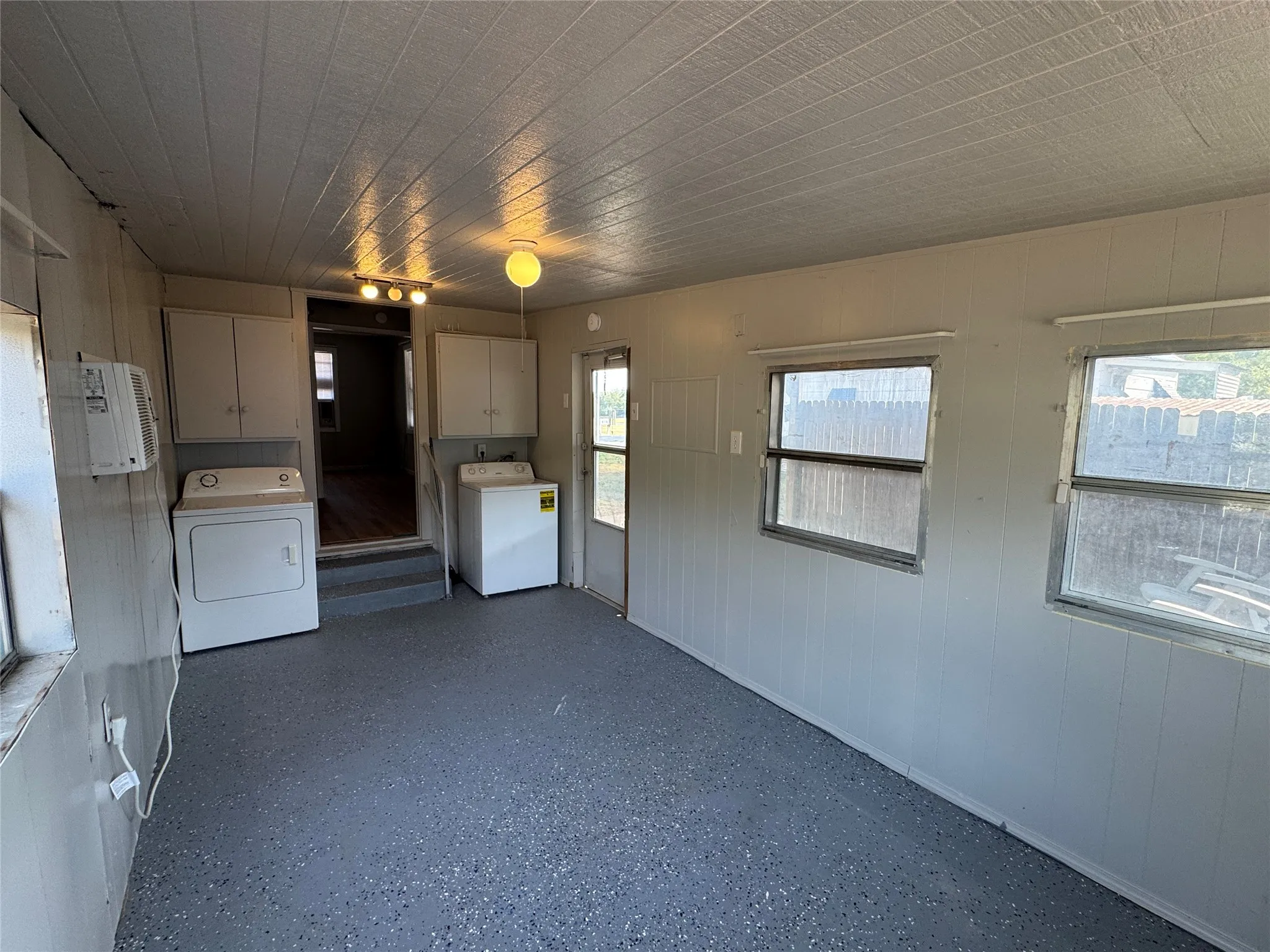 Utility space featuring speckled flooring, beadboard paneling, upper cabinetry, and multiple windows