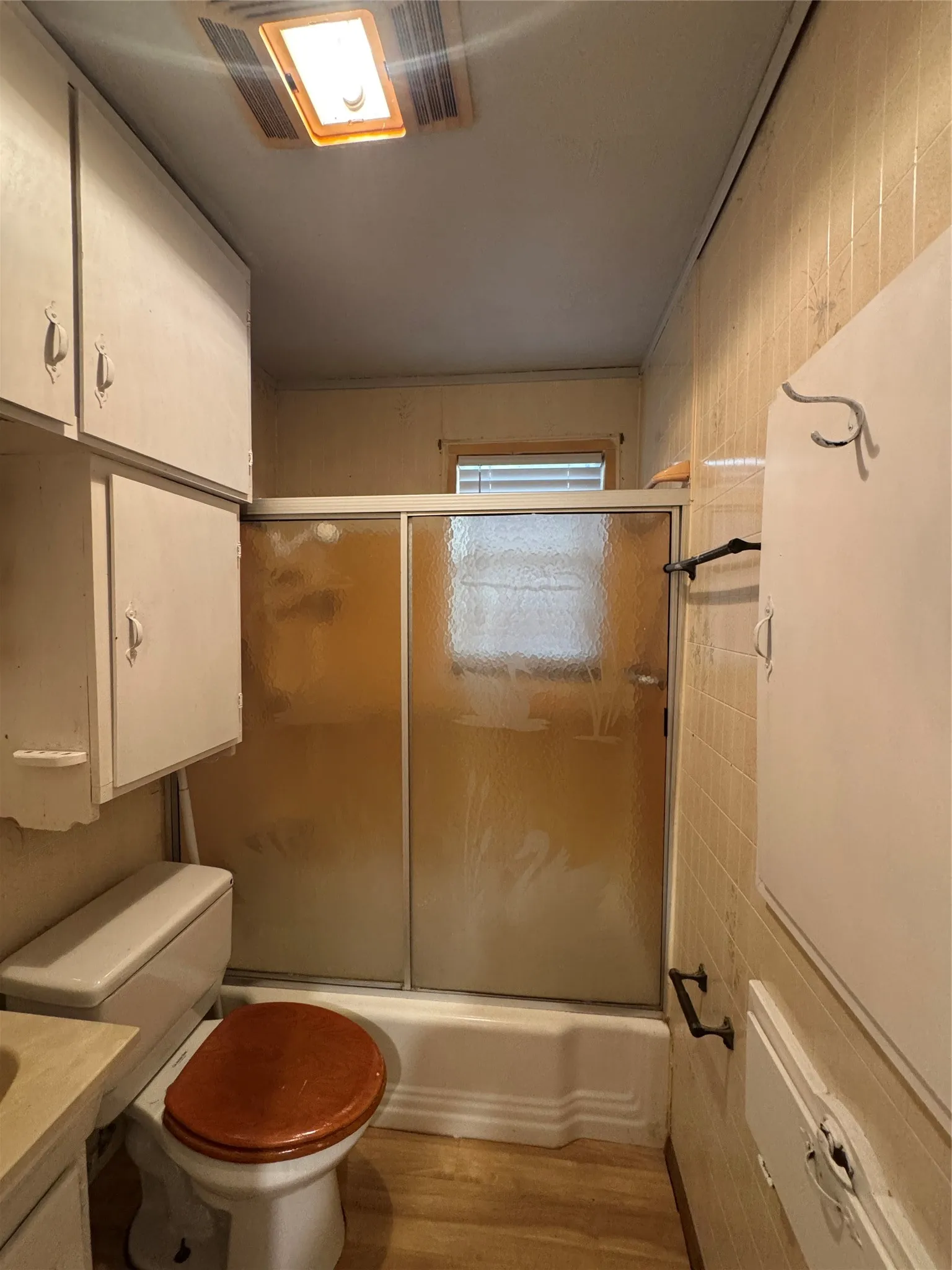 Shower enclosure with sliding frosted glass doors, built-in cabinetry, and wood-finish flooring