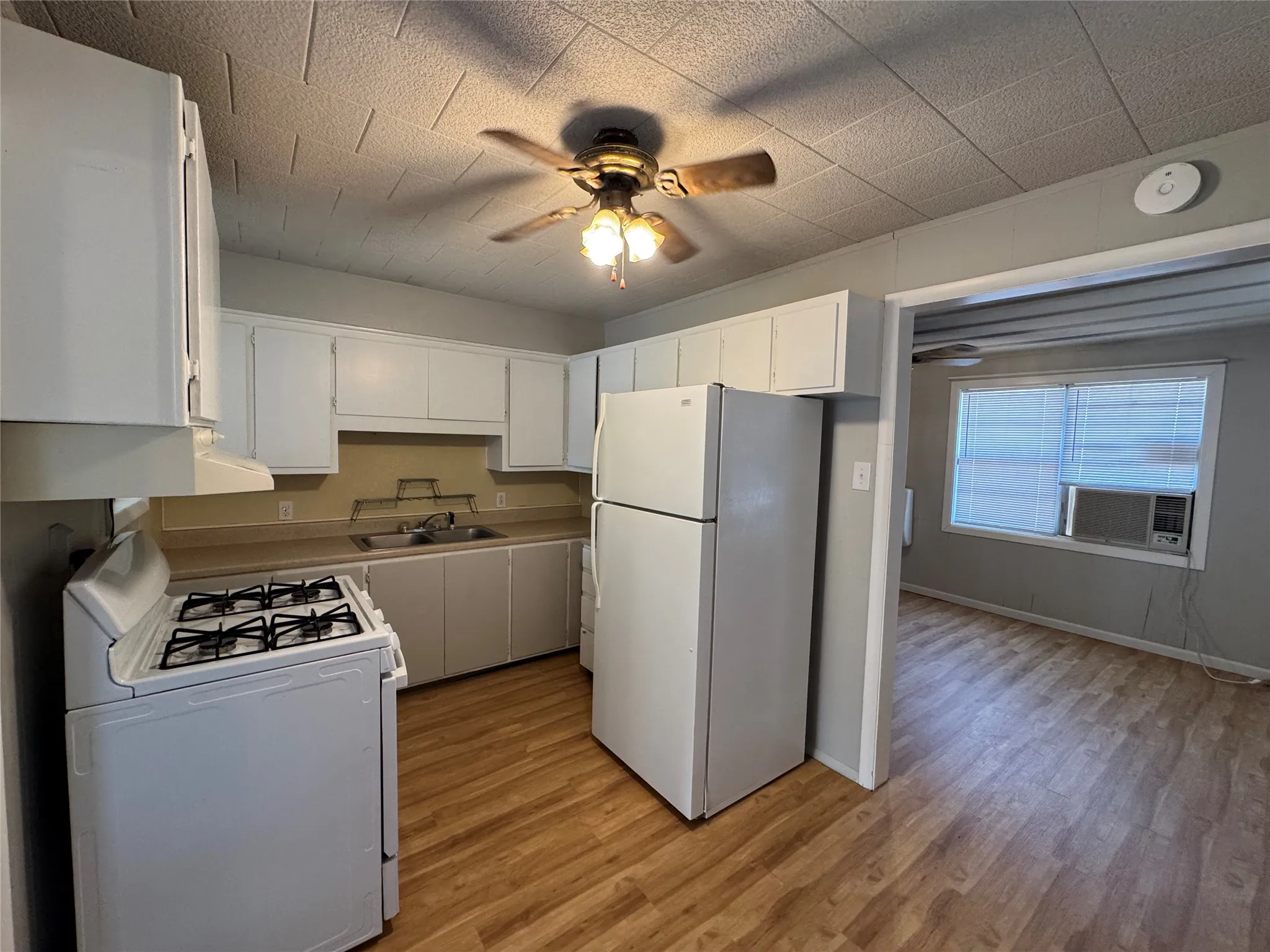 Kitchen featuring white cabinetry, wood-finish flooring, a ceiling fan, and a gas range
