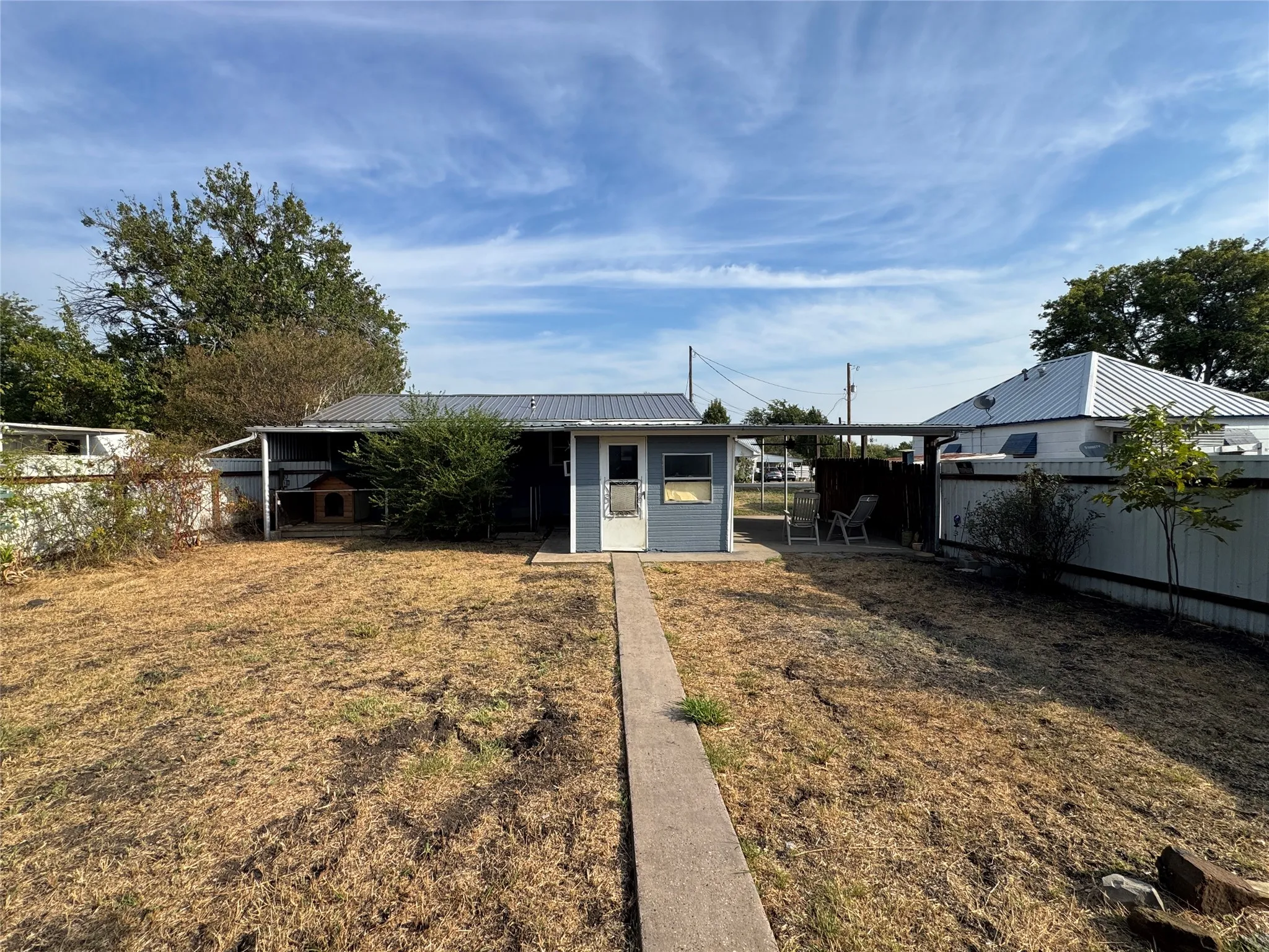 Backyard featuring a concrete pathway, a detached structure with a metal roof, and a partial privacy fence