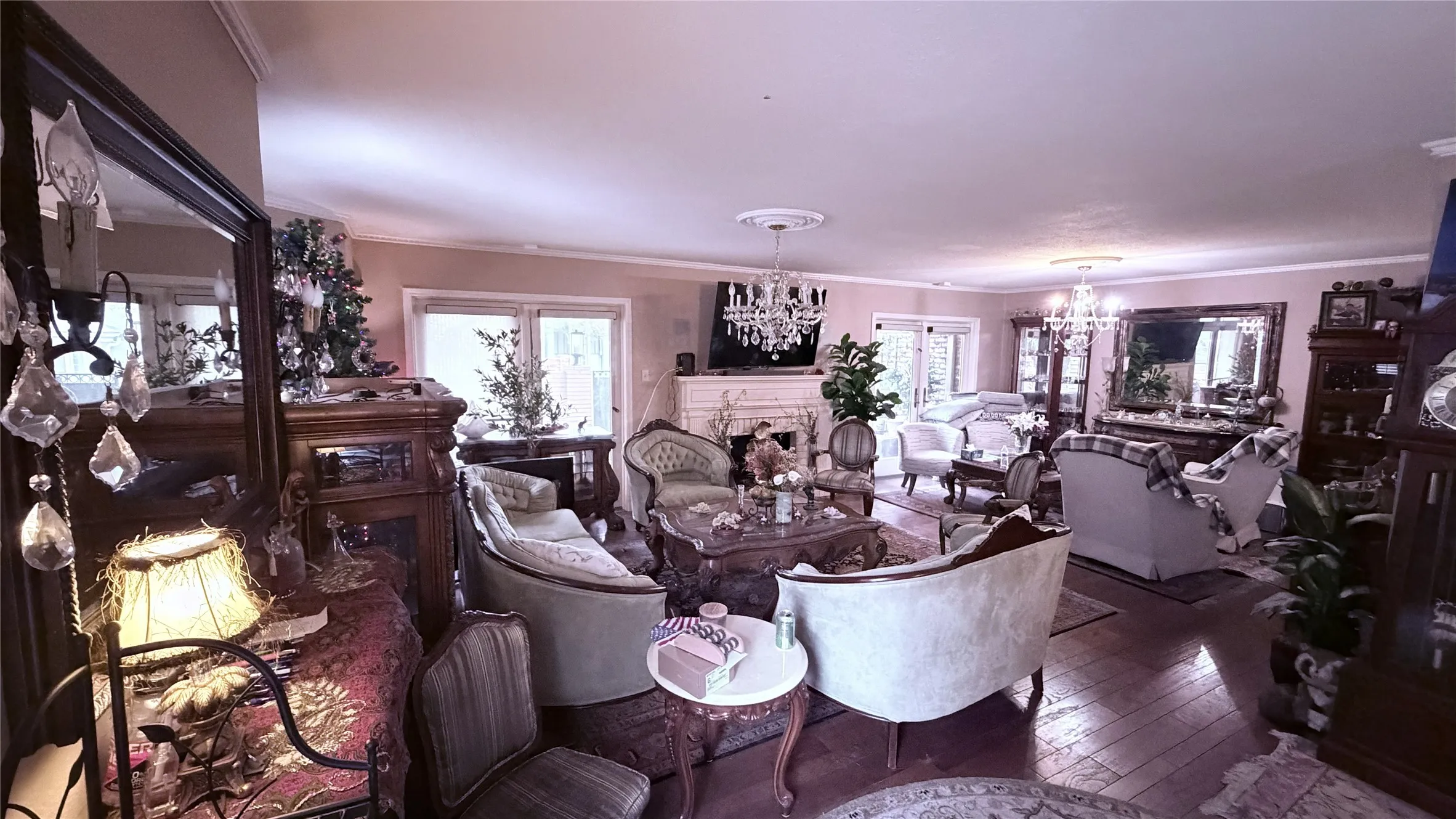 Wood-finish flooring, crown molding, double glass doors, a decorative fireplace, and crystal chandeliers